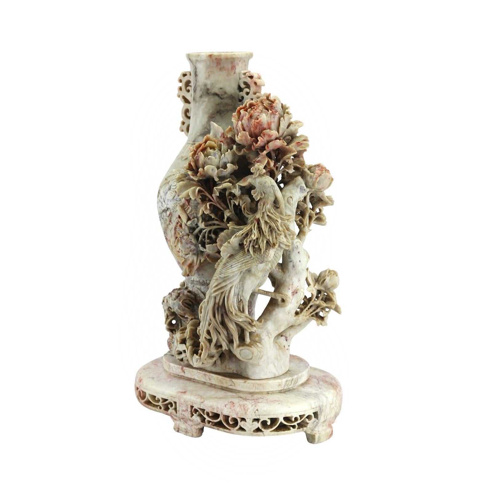 A large and dramatic early 20th century carved Chinese soapstone vase. The piece features an intricately carved phoenix resting on a branch of flowering peonies, which are accentuated by a natural red inclusion within the soapstone. The center of