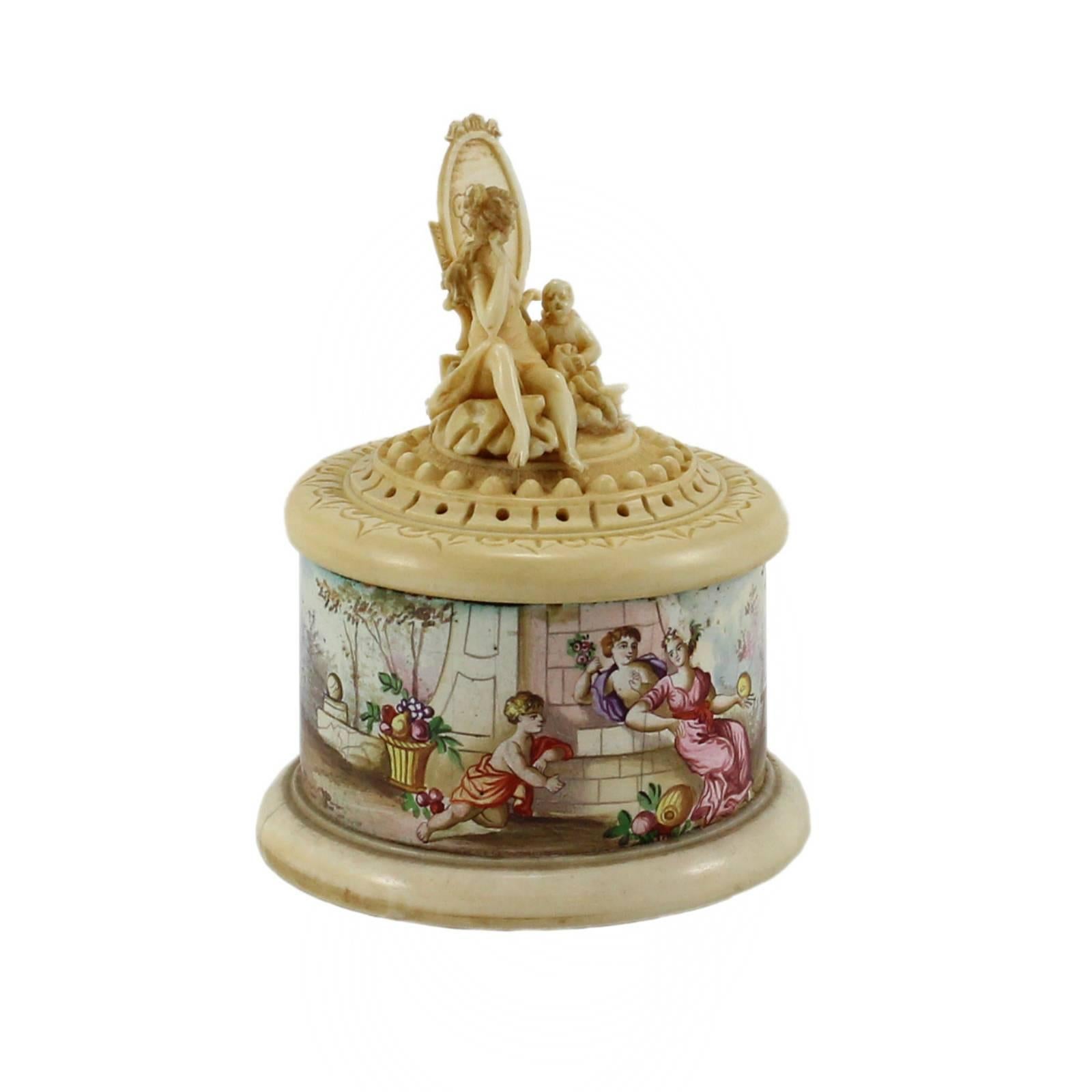 A small hand-carved ivory box and lid with intricately hand-painted enamel on the sides, depicting a scene of women in a garden. This piece originated in Austria in the 18th century.