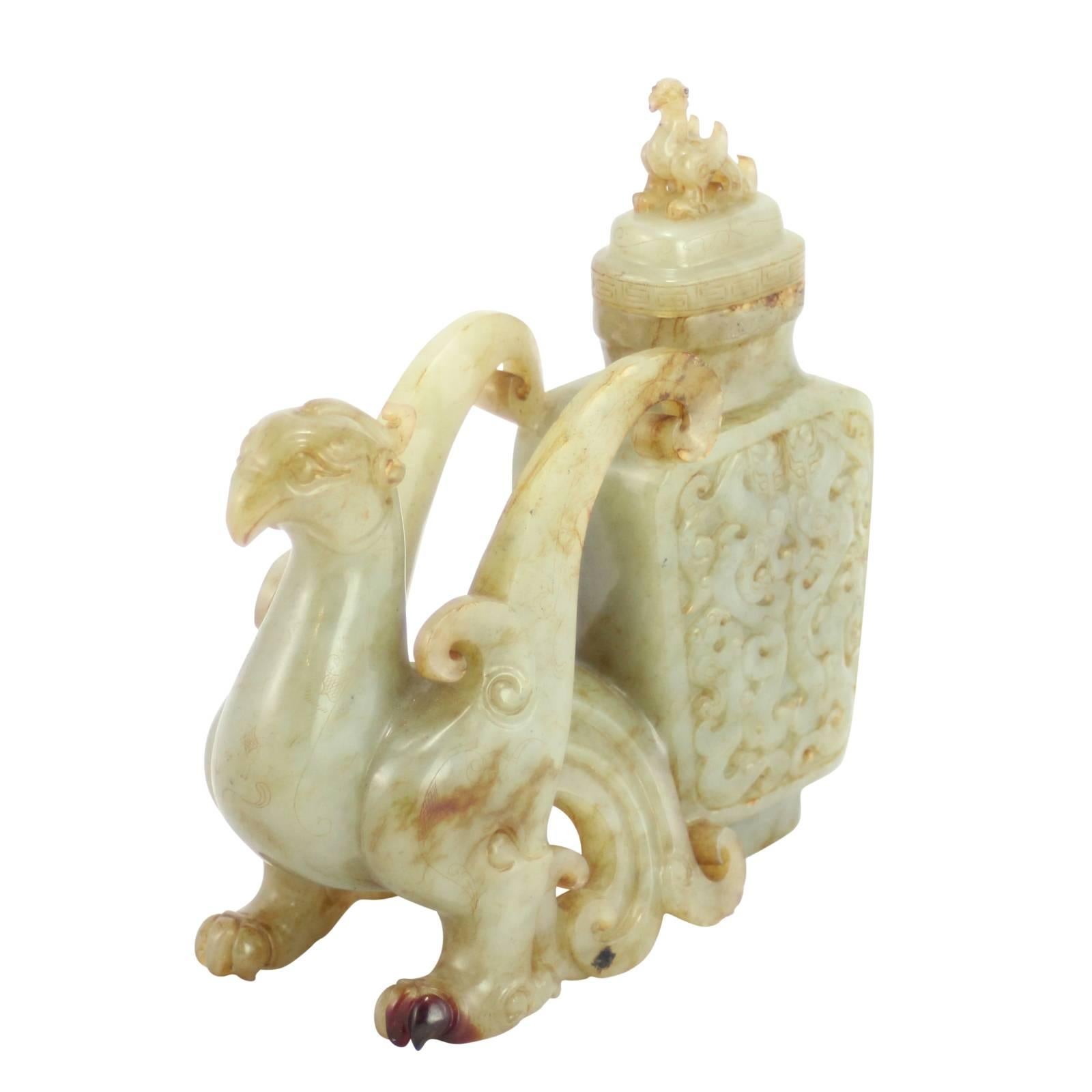 A finely carved, lidded jade vase with a figure of a Phoenix. The vase features elaborate carving and a removable lid with a finial of a Phoenix. The whole piece is crafted from pale celadon green nephrite jade with russet color inclusions.