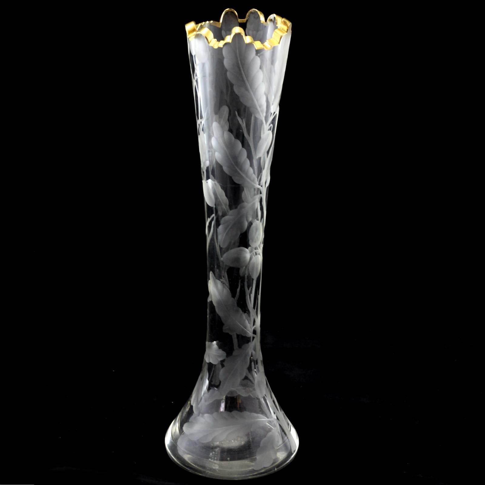 This tall slender vase features a acorn and foliate motif copper wheel etched to the exterior. The lip of the vase is accented with a thick lip of gold gilt.
