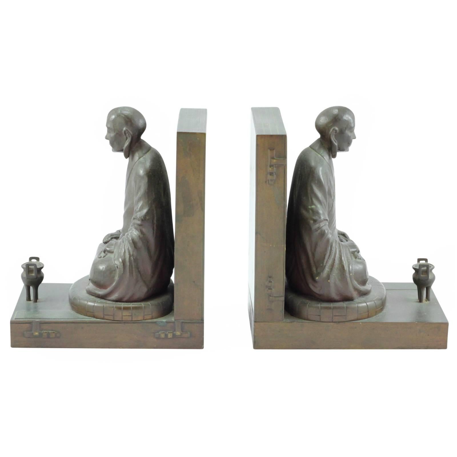 Modelled in bronze as two monks seated in meditation before tripod incense censors. They are seated upon and backed by Japanese books cast in bronze. Both have closed eyes and carry beads and scrolls in their hands.