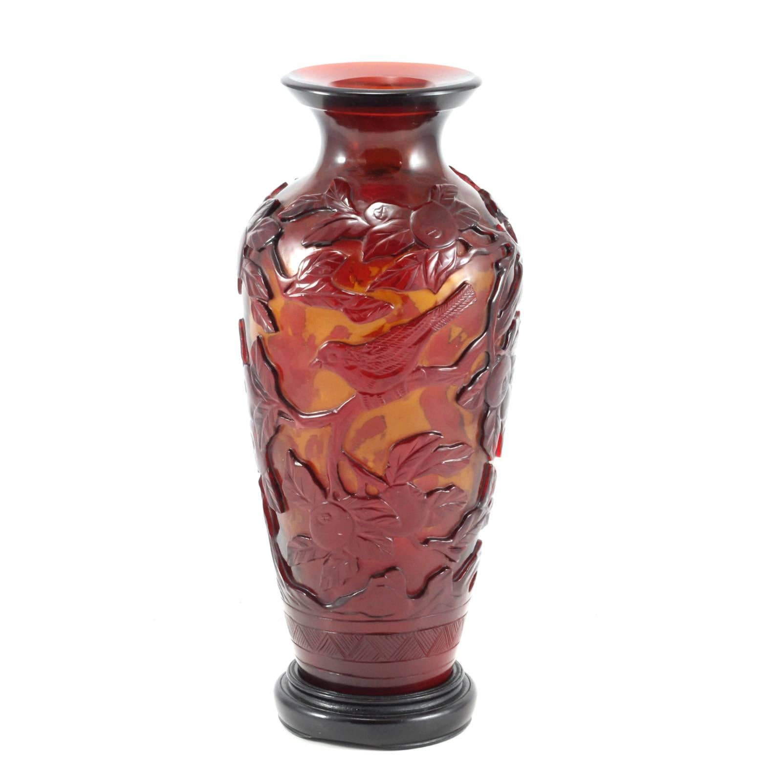 Chinese Peking glass vase featuring an amber base with scarlet glass overlay carved in a scene of birds in flight amid branches bearing pomegranate fruit. Accompanied by a fitted wooden base.