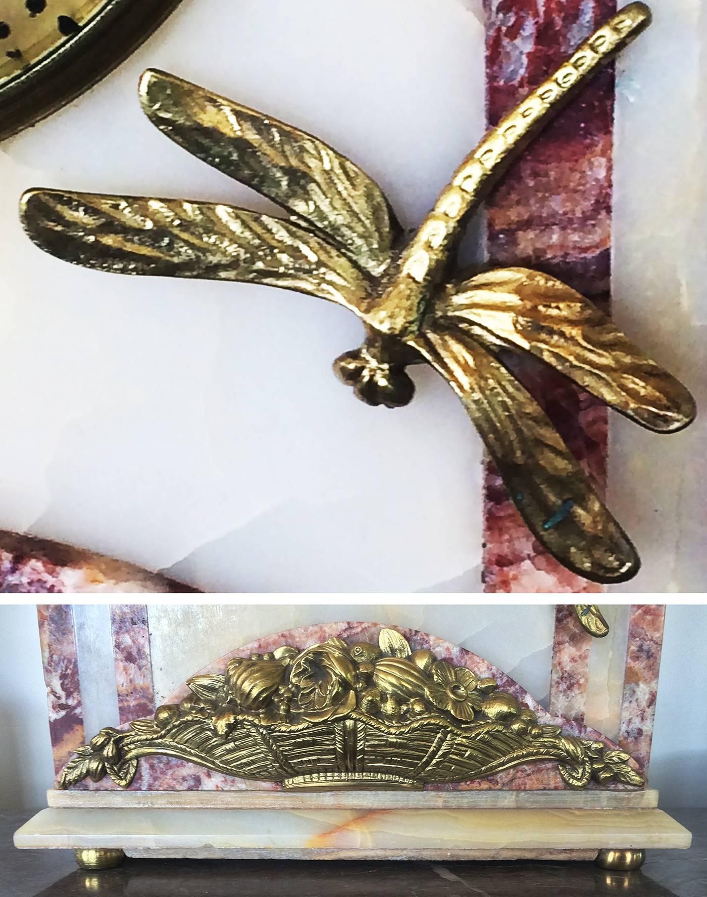 Fantastic Art Deco clock, in multi-color marble, with gilt bronze floral swage, dragonfly and bun feet. Face is also gilt, with black Arabic numerals, black dots every minute, with black triangles each 5 minute interval, with hands. The works have