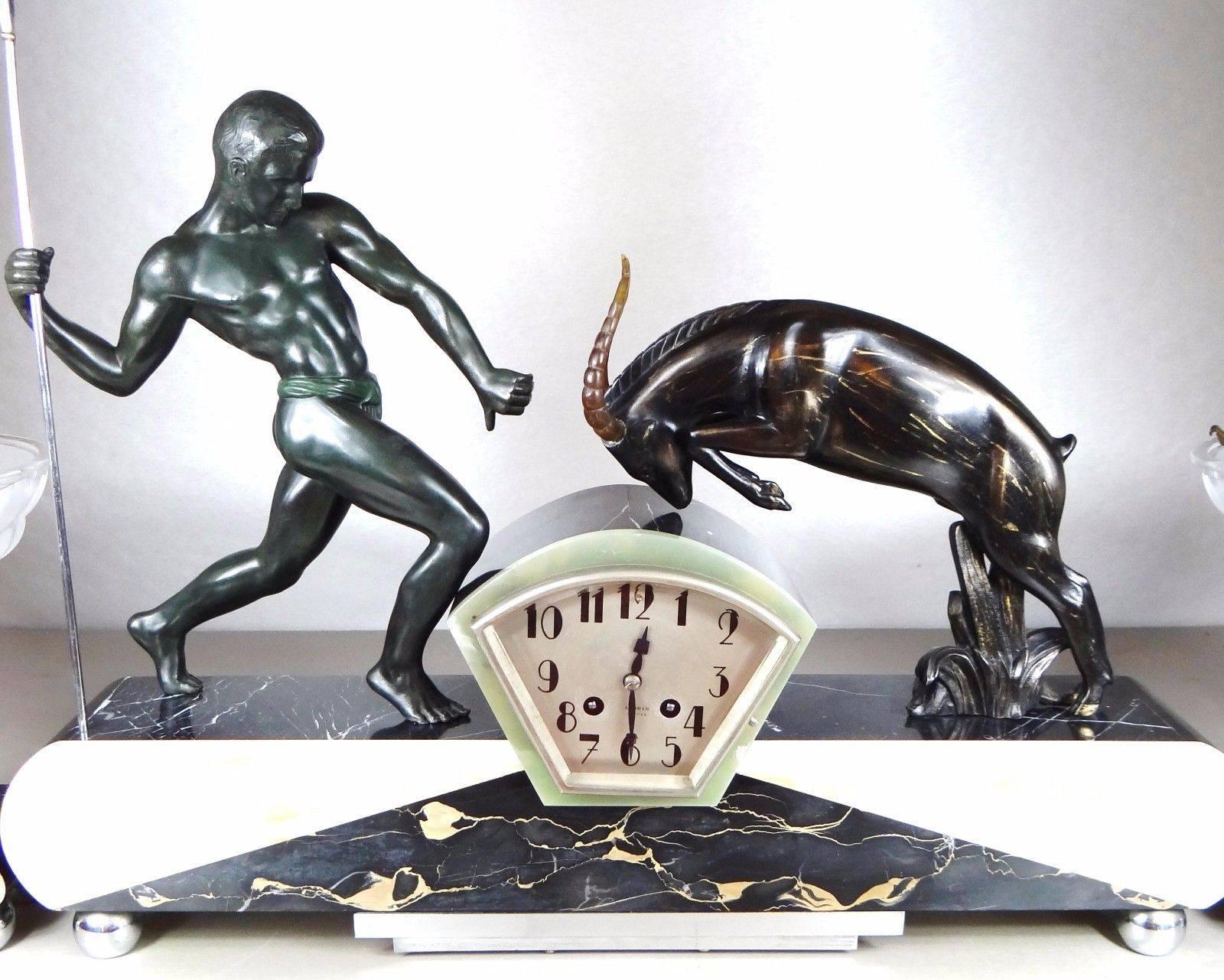 A rare Art Deco three-piece clock set, circa 1920, in working order, Signed Riolo by Salvator Riolo who was a member of the Salon Artists France and was awarded medals in 1930 Dimensions 64cm long, 12cm deep and 50cm high. The vases are 20cm long,