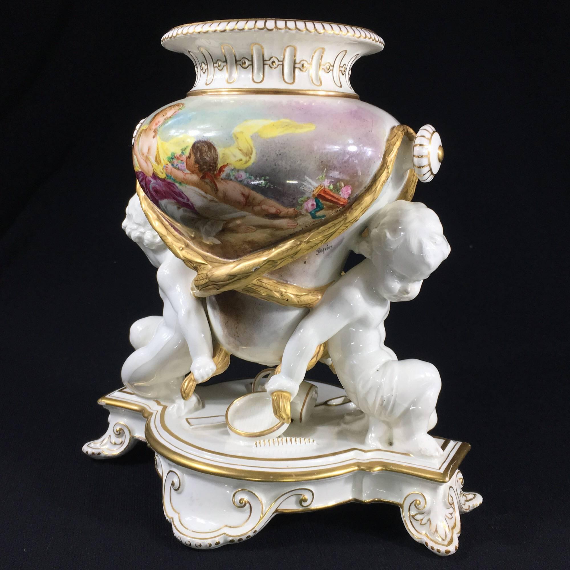 Impressive Wedgwood Queensware 'Trentham' vase, the central amphora form supported by two cherubs, a scattering of gardening tools modelled beneath, the whole on a shaped base with scroll feet, the vase painted to either side in the Continental