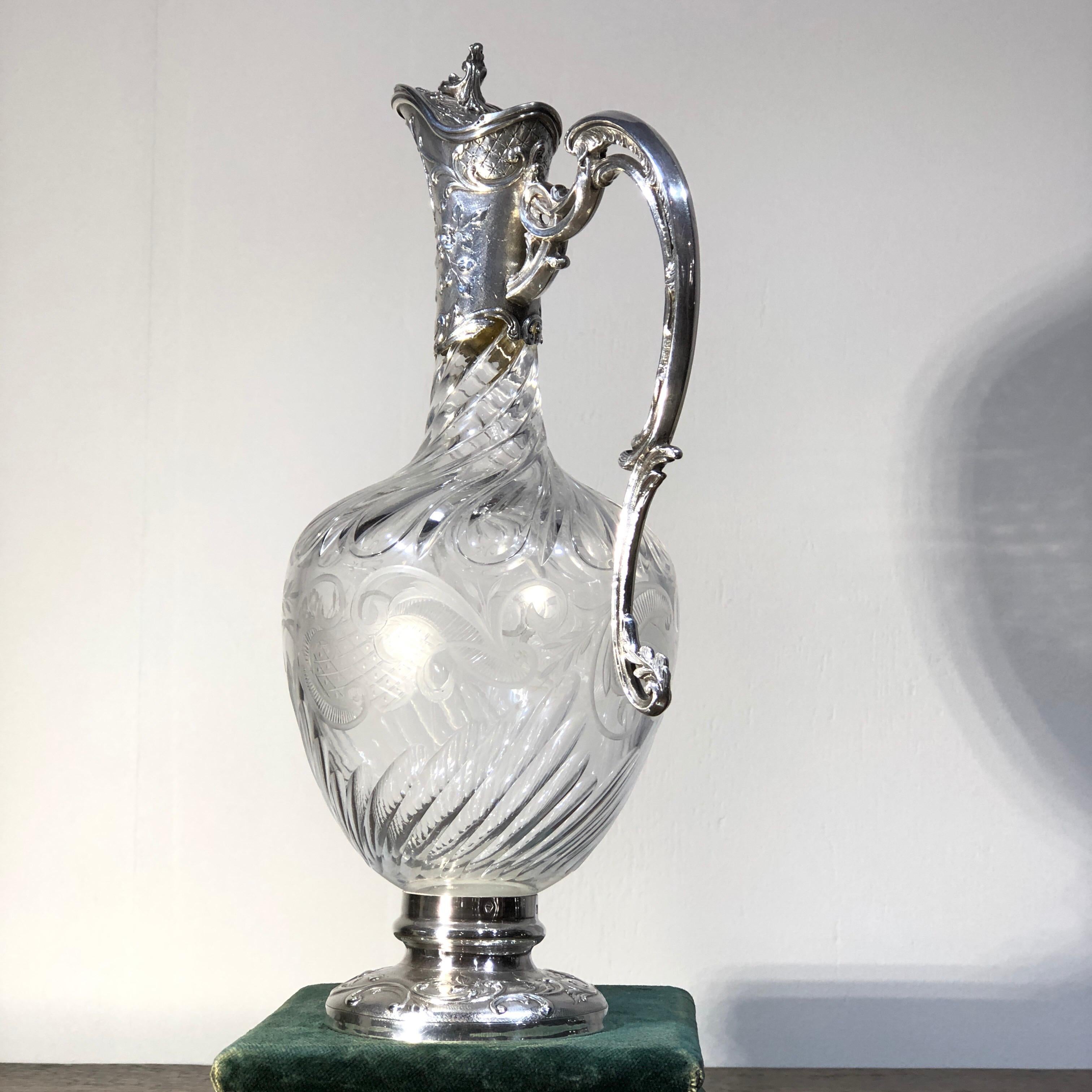 French .950 silver claret jug, the elegant silver-footed form with silver lidded spout and handle engraved and embossed in an elaborate rococo manner, the quality crystal body with spiral cut fluting to the narrow neck, with scrollwork cutting to