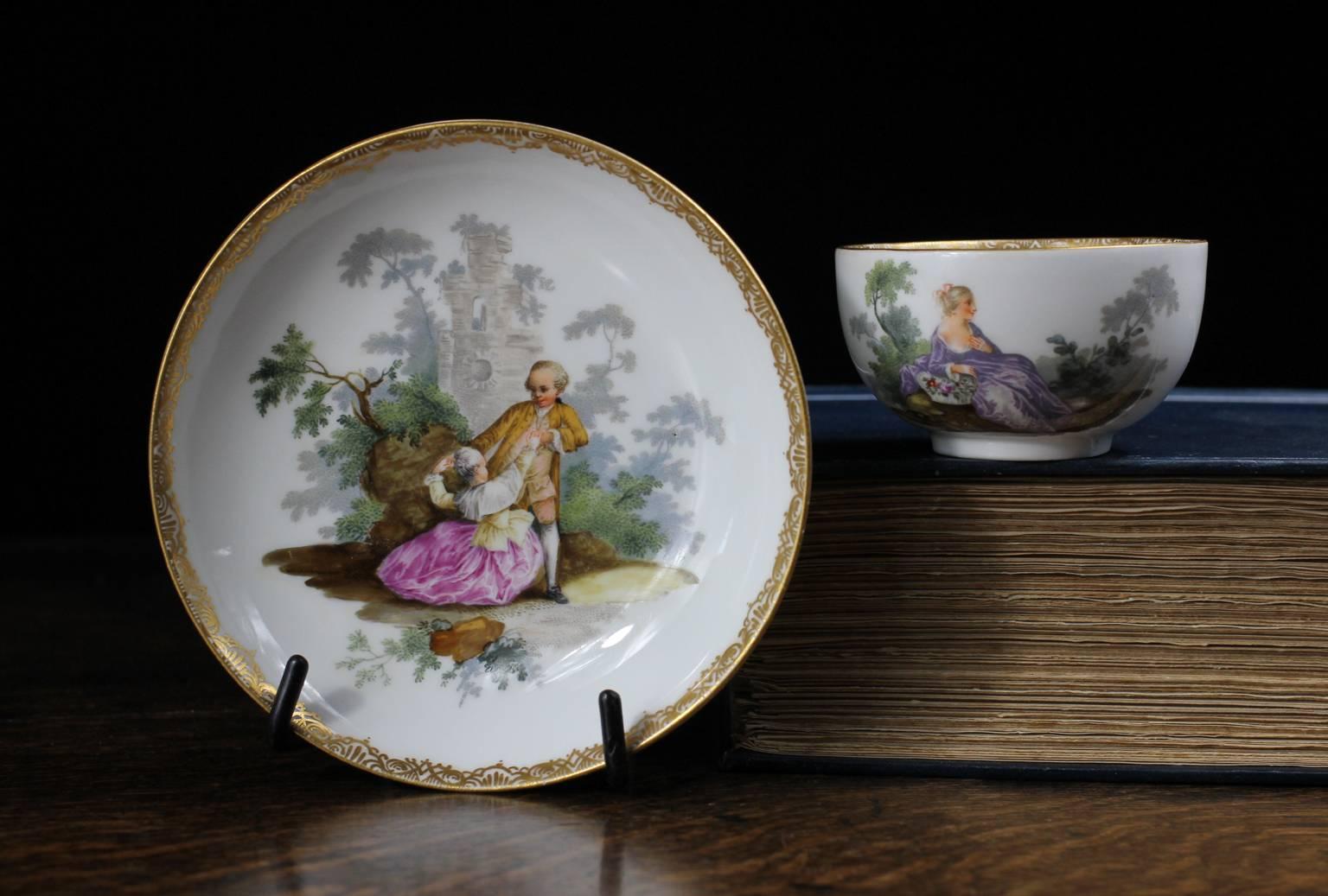 Meissen teabowl and saucer, superbly painted with large-scale Watteauesque scenes of couples in garden, within a fine gold tracery border. 
Blue crossed swords and dot mark, 
circa 1770.
