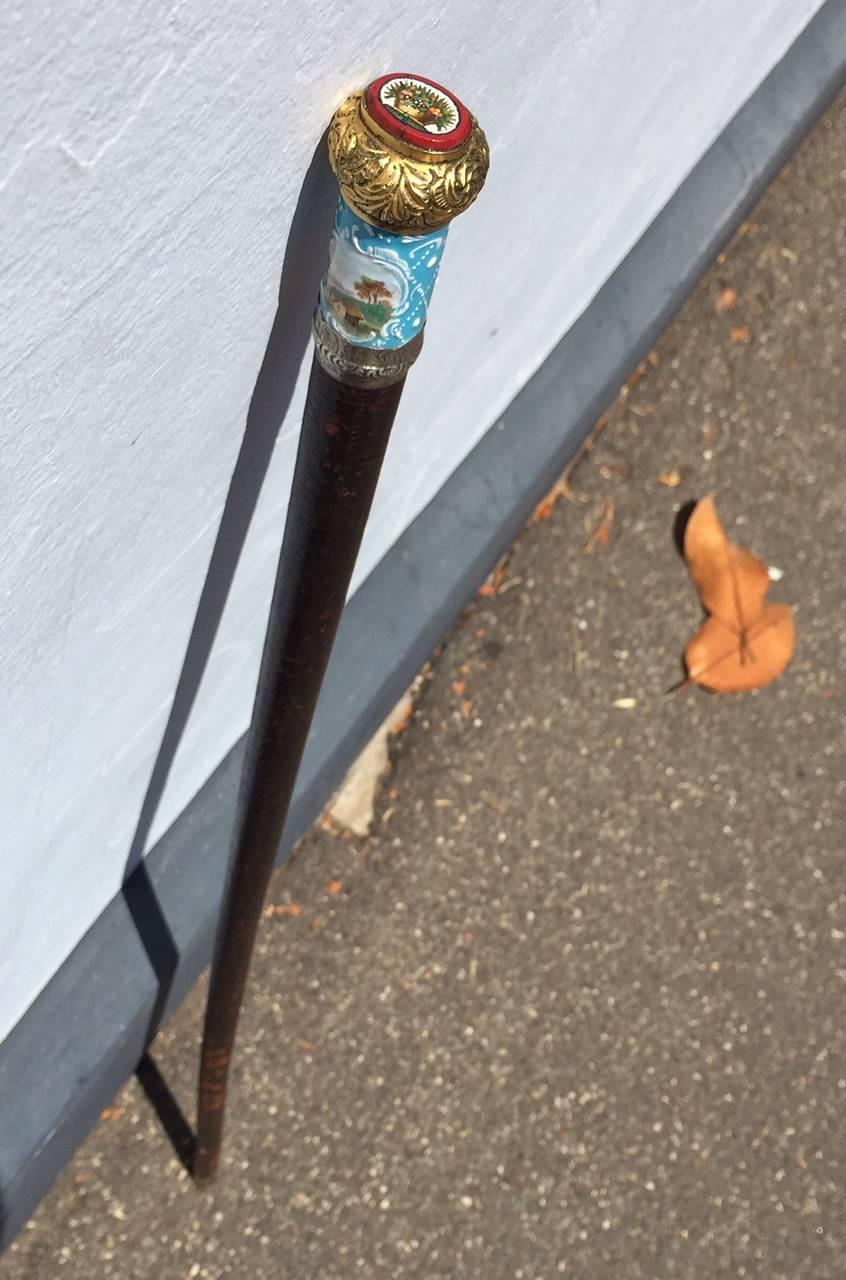 Superb quality English cane, the shaft bound with cord and lacquered, the head with a South Staffordshire enamel collar with a countryside scene reserved on a blue diaper ground, enclosed with a lower silver band tooled with foliate designs and an