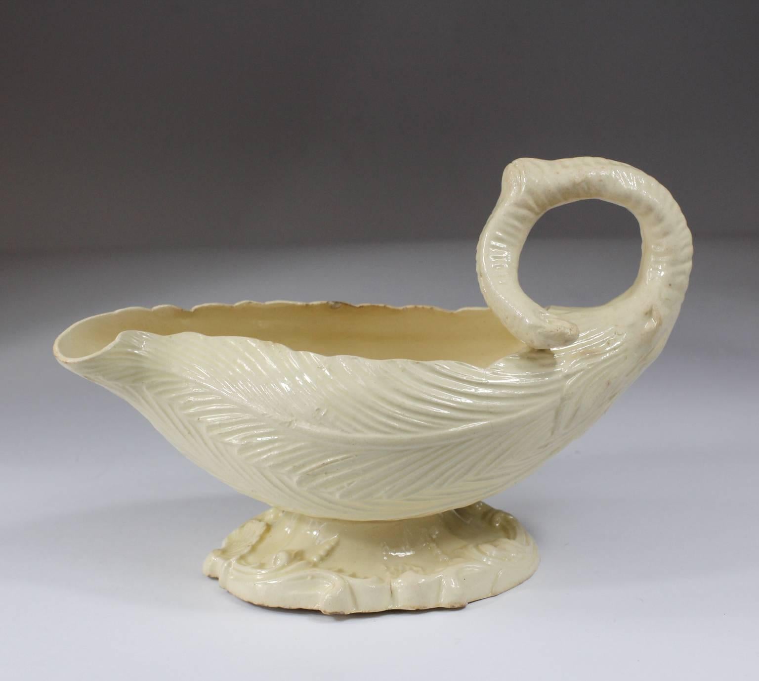 Rare English creamware sauceboat, of Rococo silver form, the upper vessel modeled as interlocking cos lettuce leaves with a scrolling stalk handle, the base with Rococo scroll moulding and a central scallop shell motif. 
Unmarked, circa 1760.