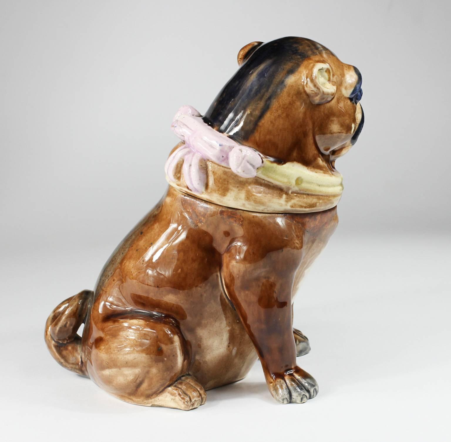 English majolica seated pug dog with lift-off head, for use as a tobacco box, realistically modelled wearing a collar with a pink bow and bells,
circa 1870.