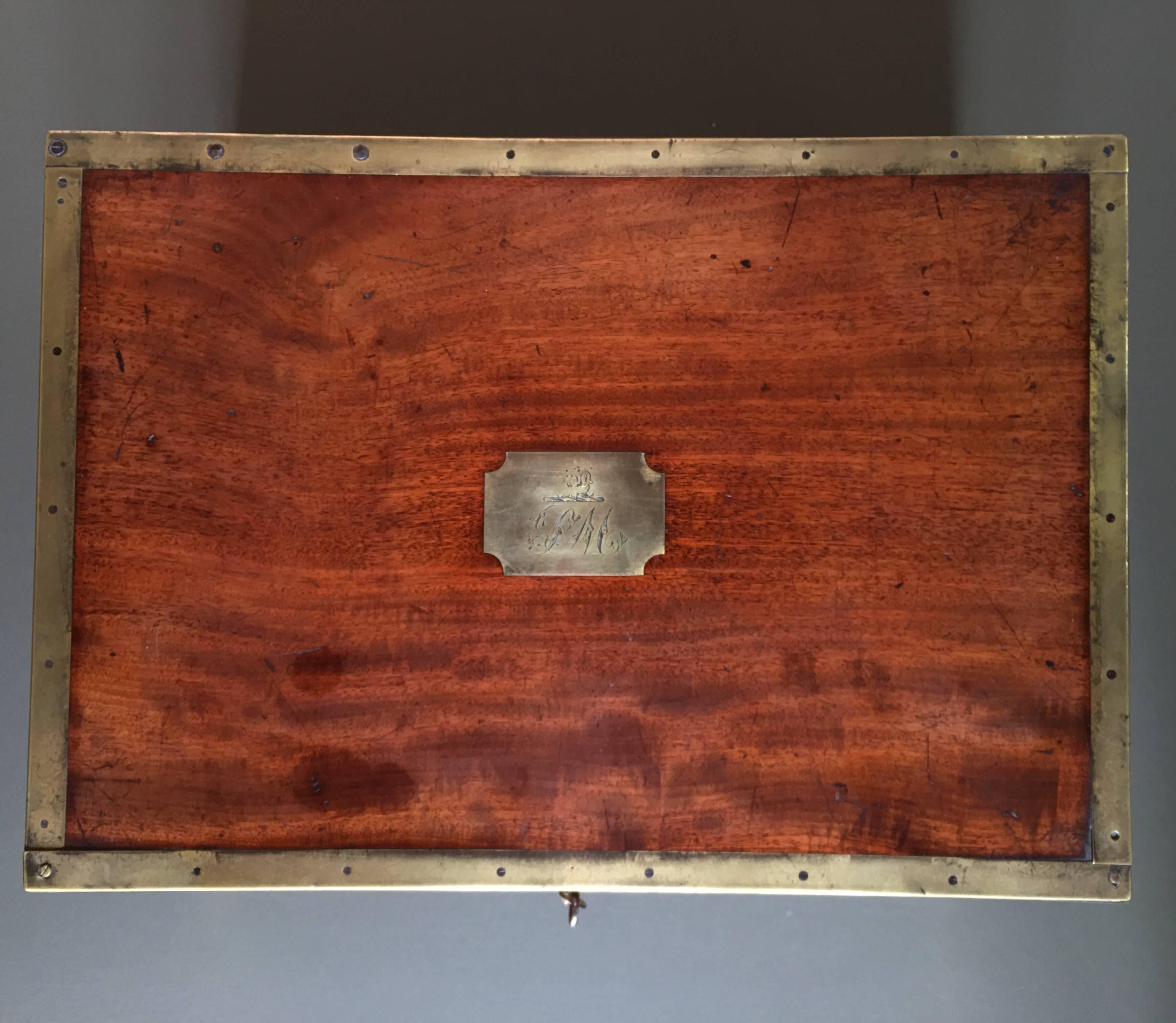 Major-general sir Peregrine Maitland's mahogany document box, with recessed handles and reinforced brass edges, the central plaque inscribed 'PM' beneath a family crest, with central leather lined compartment and hinging lid compartment, a slide out