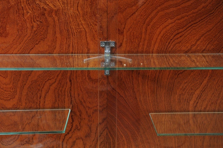 Beautiful wall mounted showcase cabinet with built-in lighting, probably made in the 1950's.
This showcase comes from the inventory of a high end optician. 
It has five glass shelves behind its two sliding glass doors.