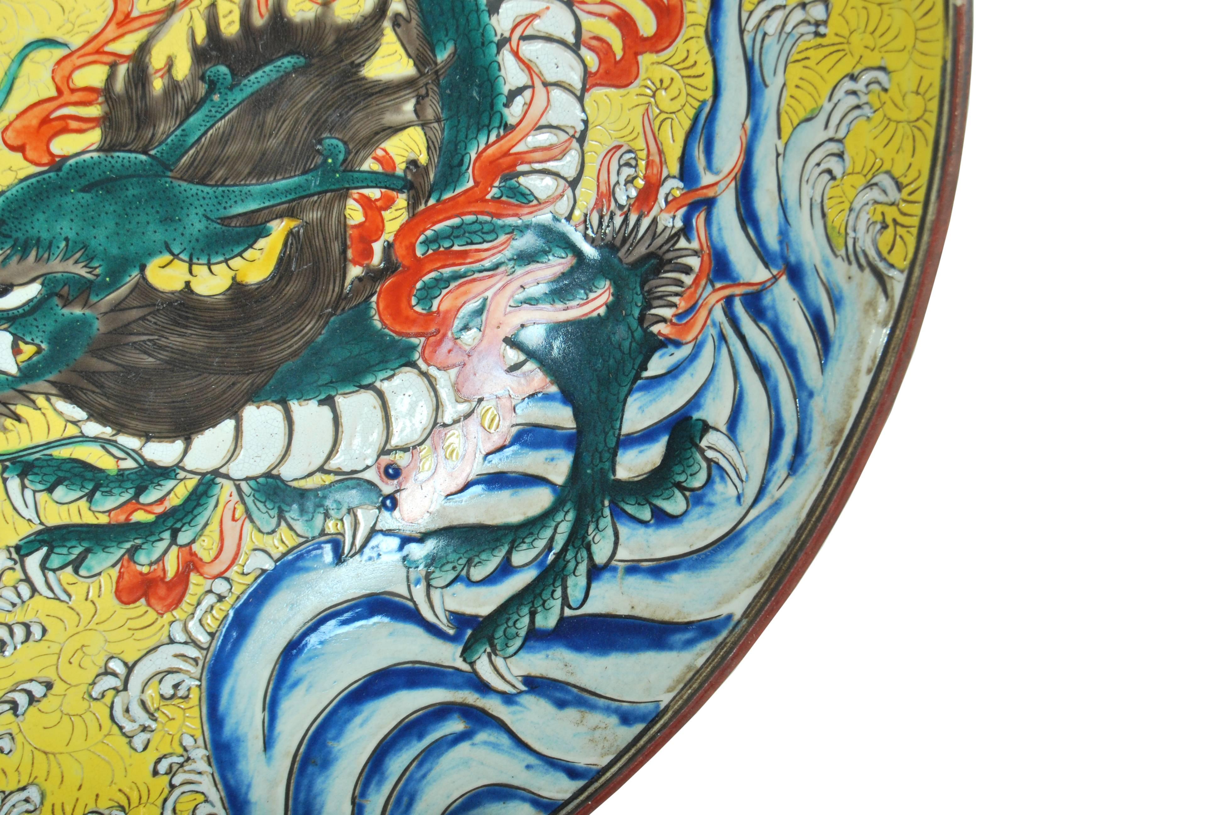Large antique Japanese kutani porcelain charger decorated with a well painted design of a writhing dragon surrounded by flames and set against a vibrant yellow glazed ground of karakusa scrollwork above a sea of churning waves, the whole executed in