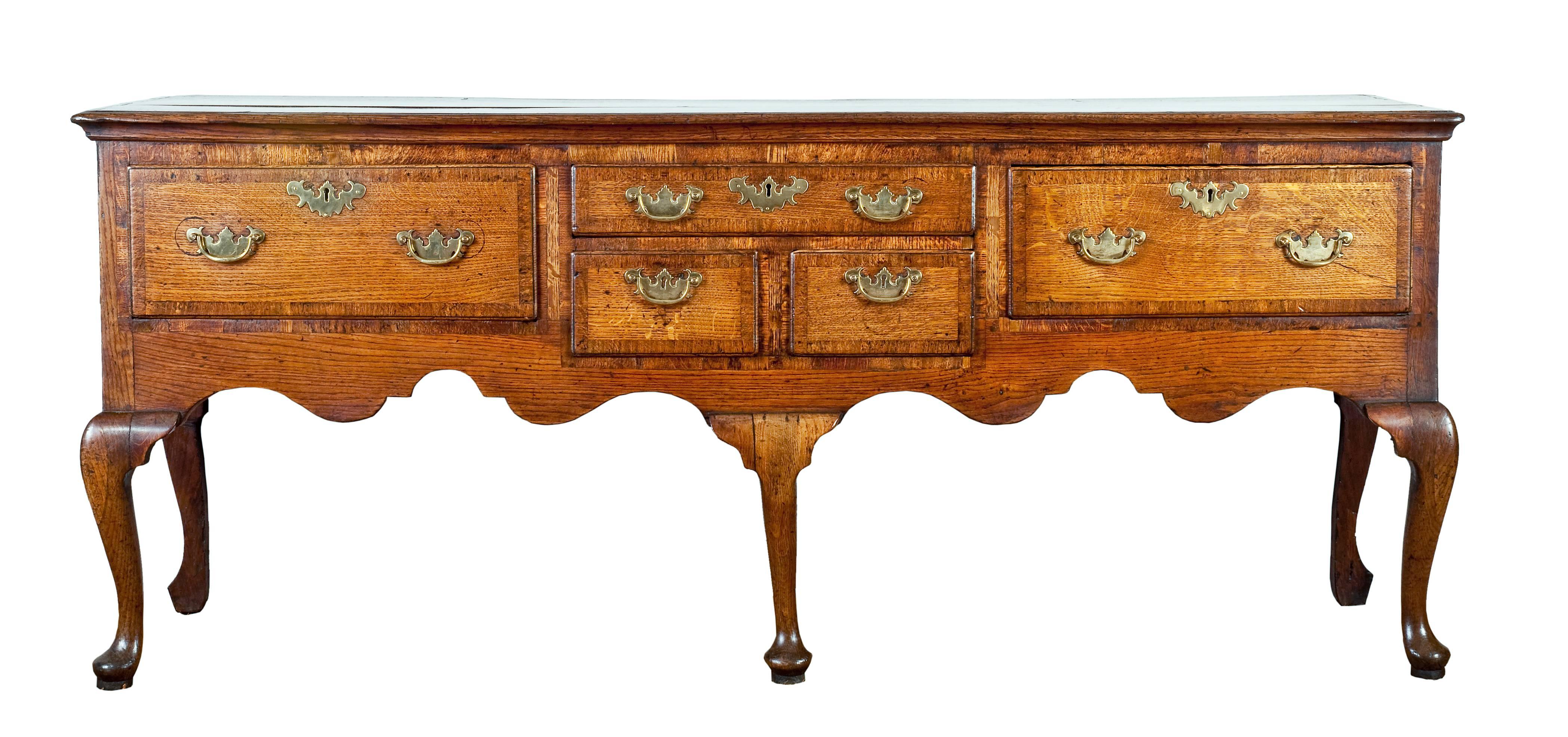 An 18th century English oak dresser base - UK1788.

Having a boarded crossbanded top above a shallow central drawer above two short drawers, flanked by two deep drawers, all crossbanded. With a shaped apron, raised on five attractive cabriole legs