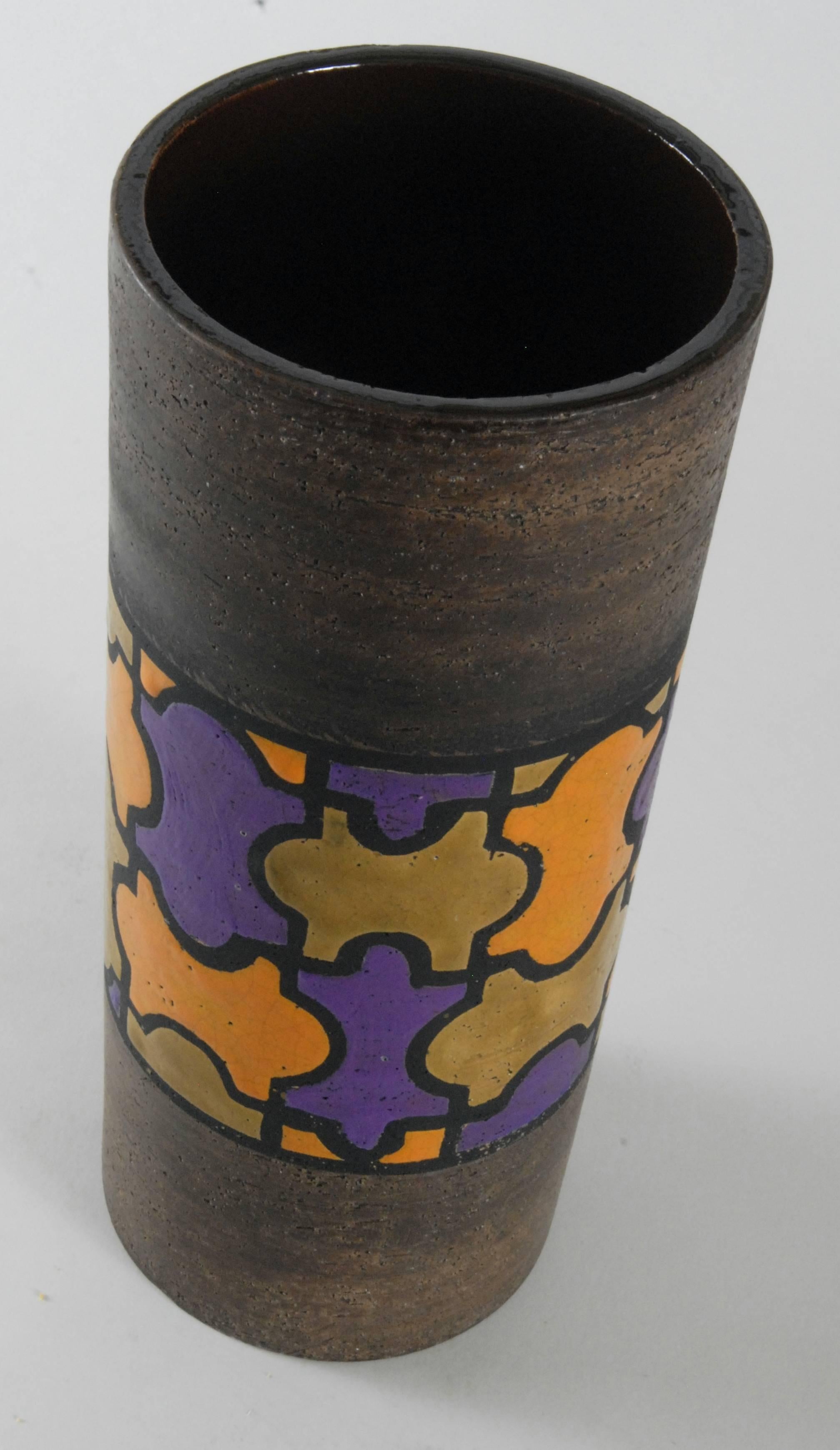 A large jig saw type pattern to the centre of a manganese finished cylindrical body.
The purple, orange and yellow ochre gloss glazes counterpoint with the semi-matte brown body. A substantial piece in excellent condition.