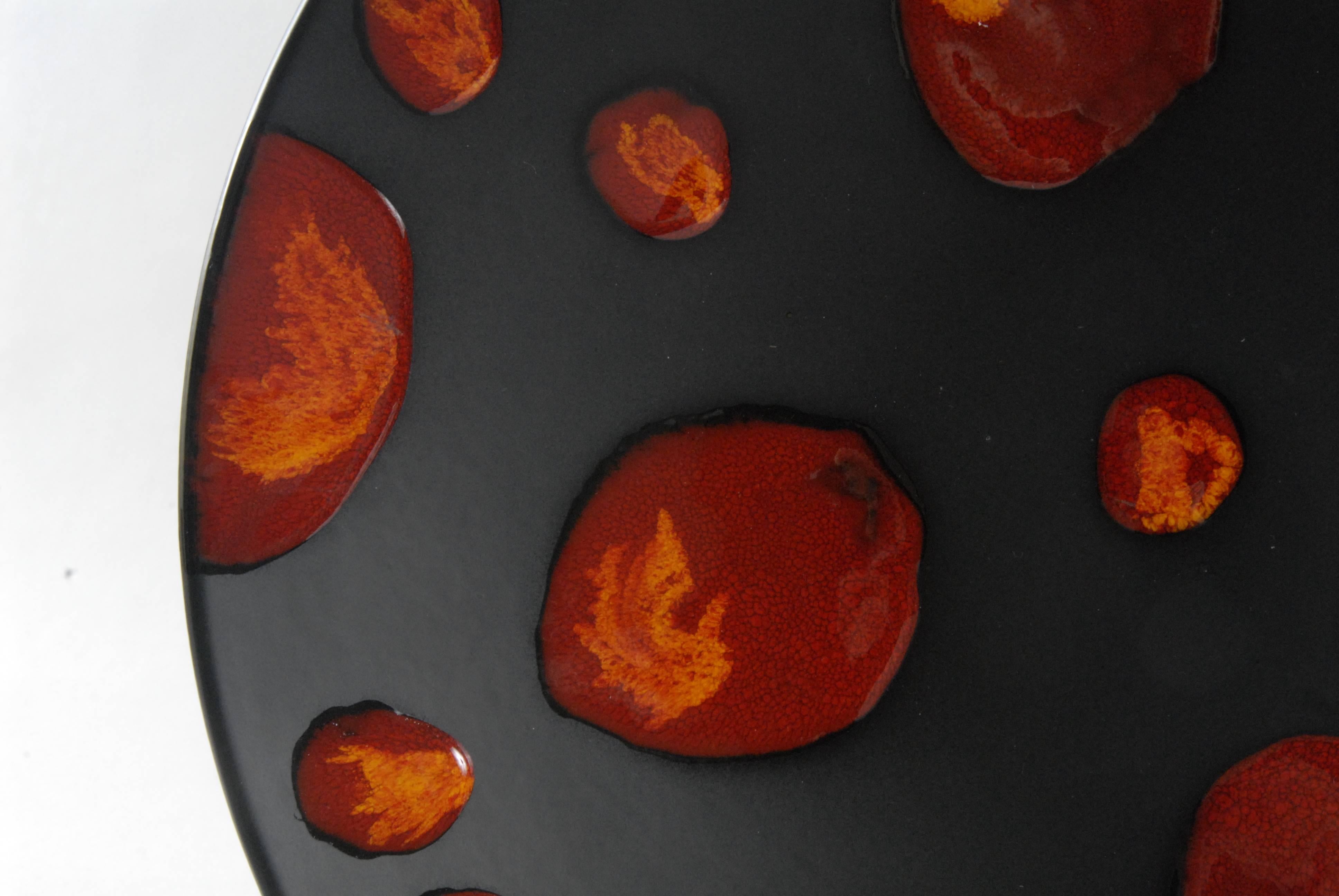 A large charger with the 'Living Glaze' technique in the 'Galaxy' pattern. Matt black background enhances the red and orange 'meteorites' Signed on the back, 'AH'.