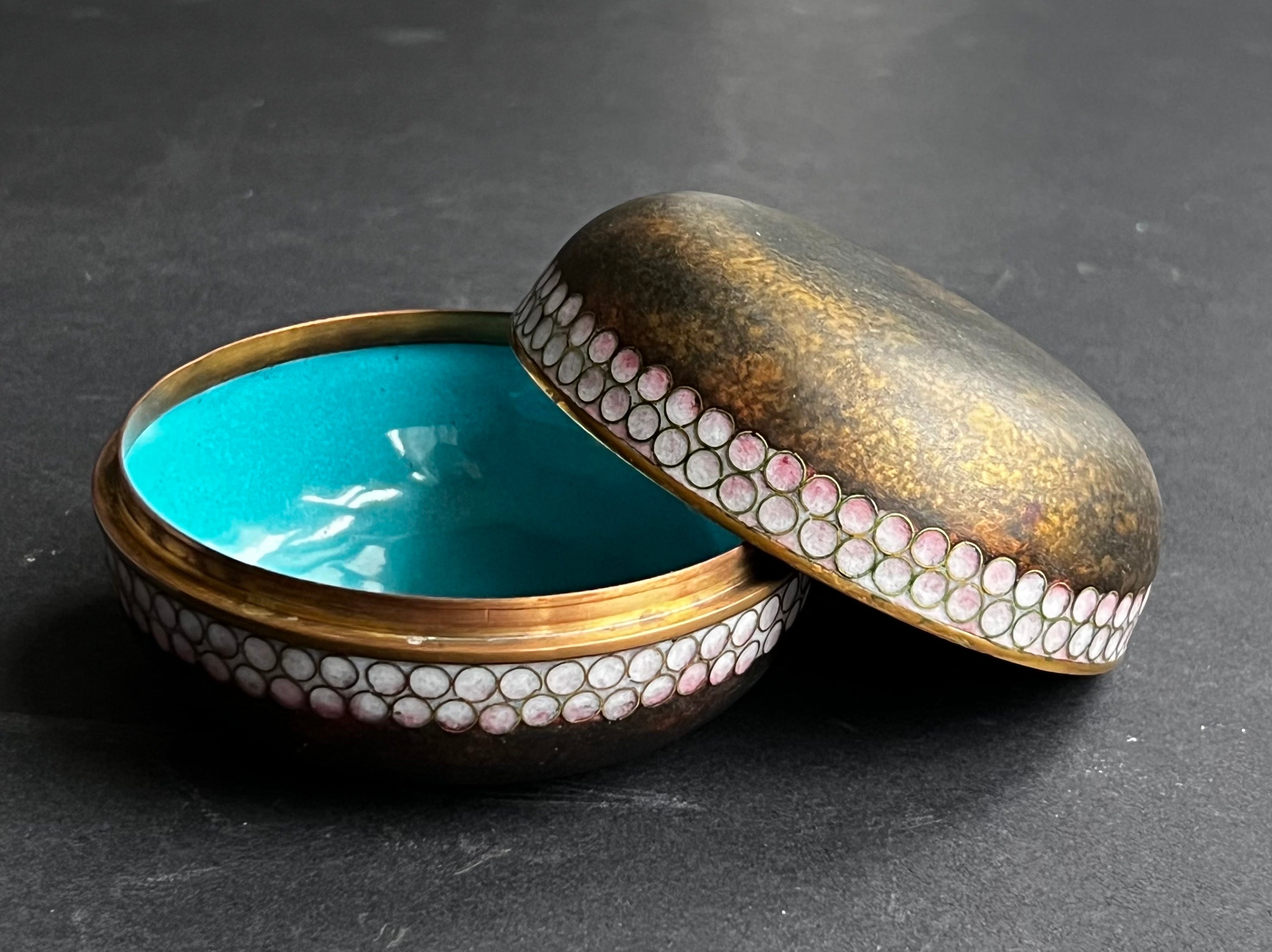 Cloisonné lidded box attributed to jeweller Käthe Ruckenbrod (1905 - 1989). Germany, mid-20th century.

The box is rounded, smooth and tactile to top and bottom; the enamel is golden brown with pale pink details to the outside, and rich turquoise