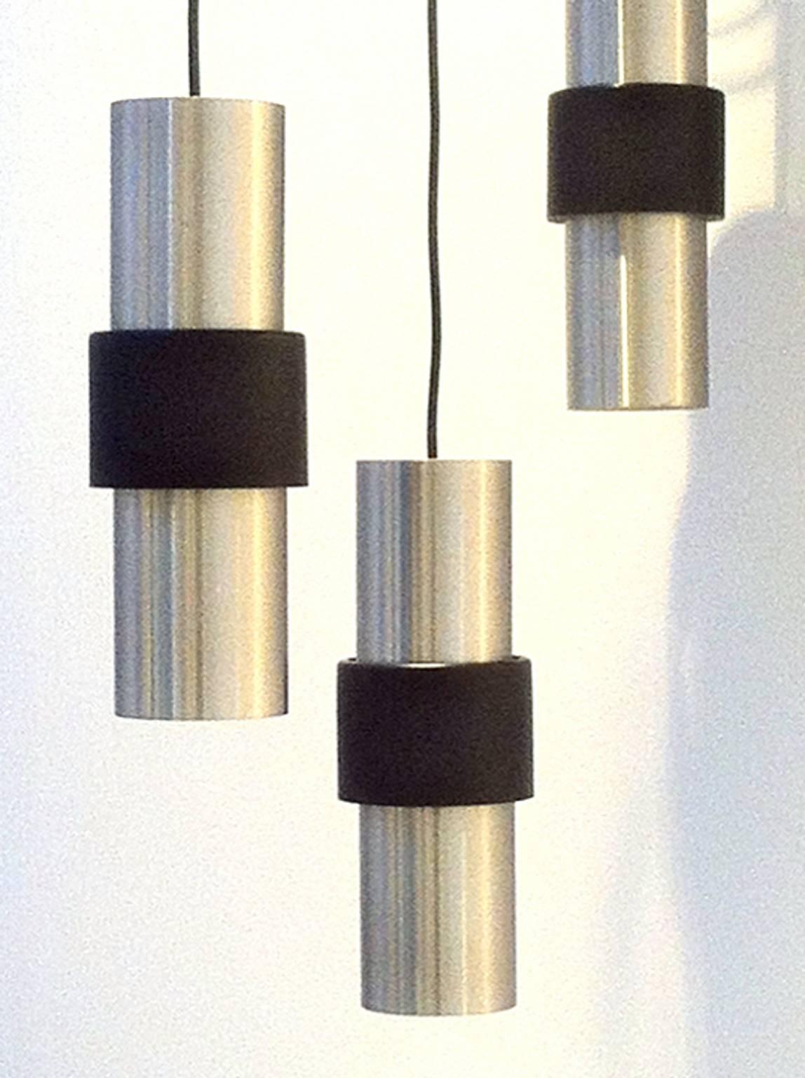 Set of three elegant pendant lights by RAAK of the Netherlands, 1960s.

These lights are made of brushed aluminium with a black lacquered band which floats away from the body allowing light to filter both up and down (this also provide access to