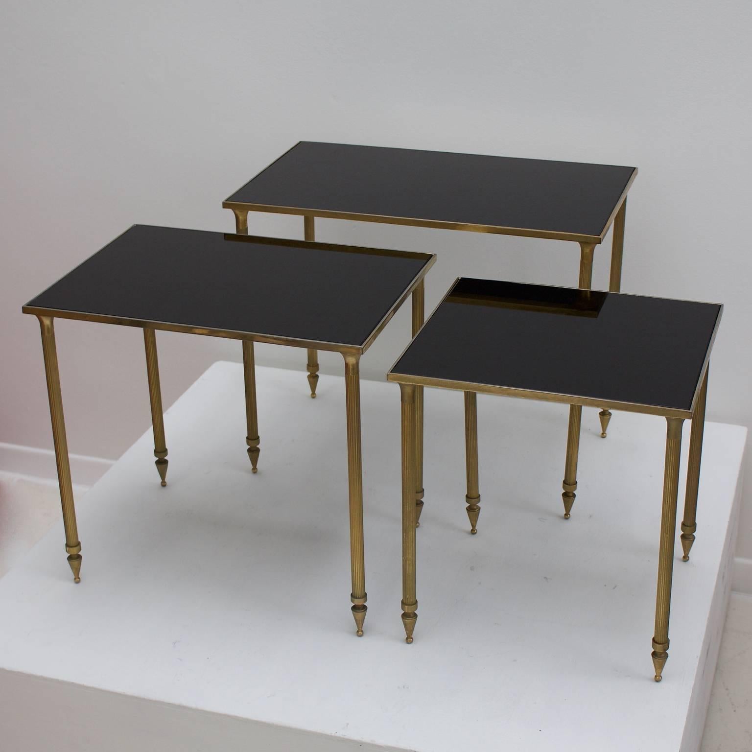 Set of three nesting tables with black glass tops and brass-finished frames, in Hollywood Regency style. European, probably 1970s.

The tables are in very nice vintage condition with an attractive overall patina in line with age. There is light