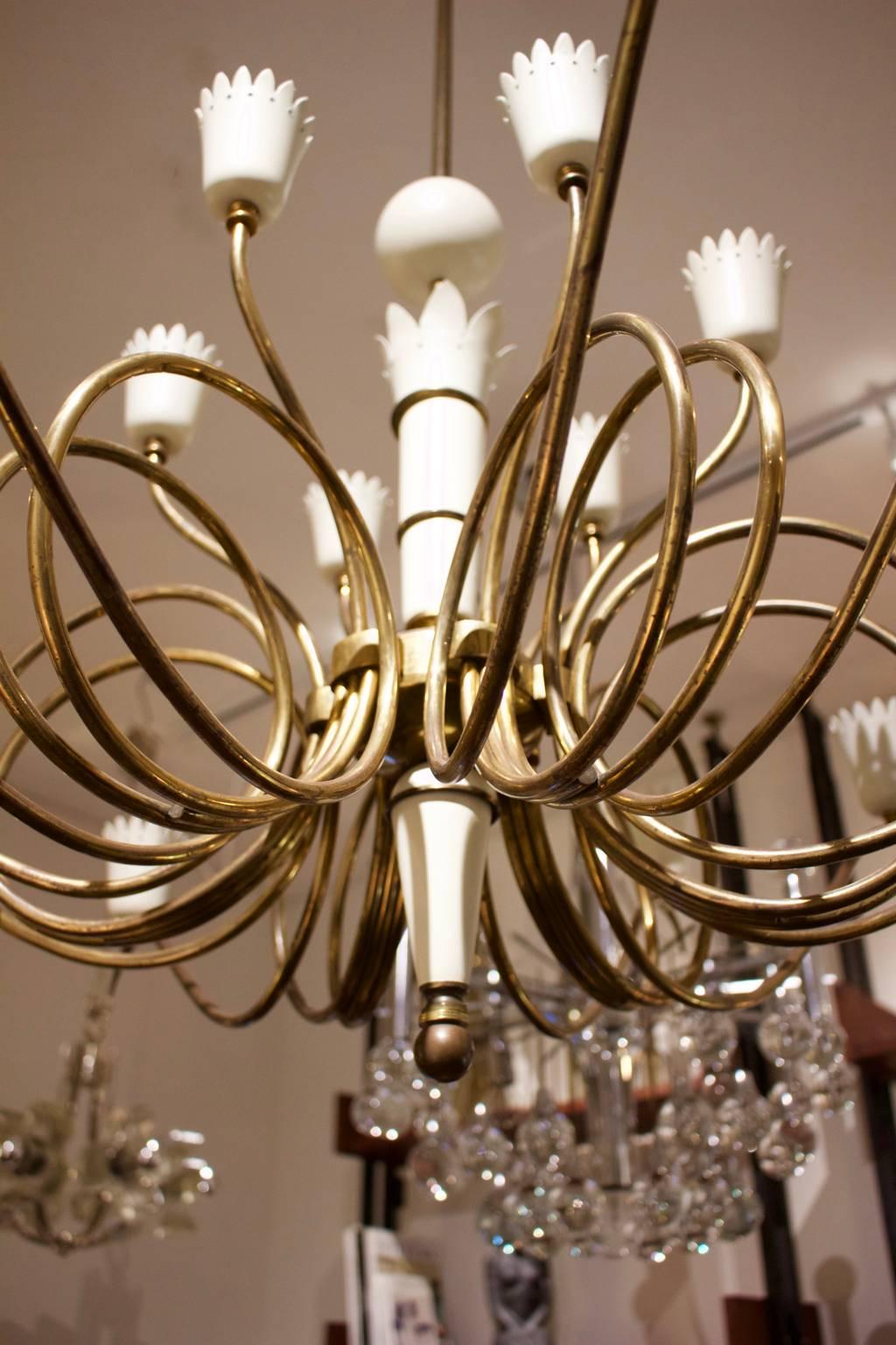 Large chandelier of brass with painted details. Italian mid-20th century, probably early 1950s.

The chandelier comprises six sections, each with three curved and looped arms ending in crown-shaped cones, painted in off-white, giving 18 lights in