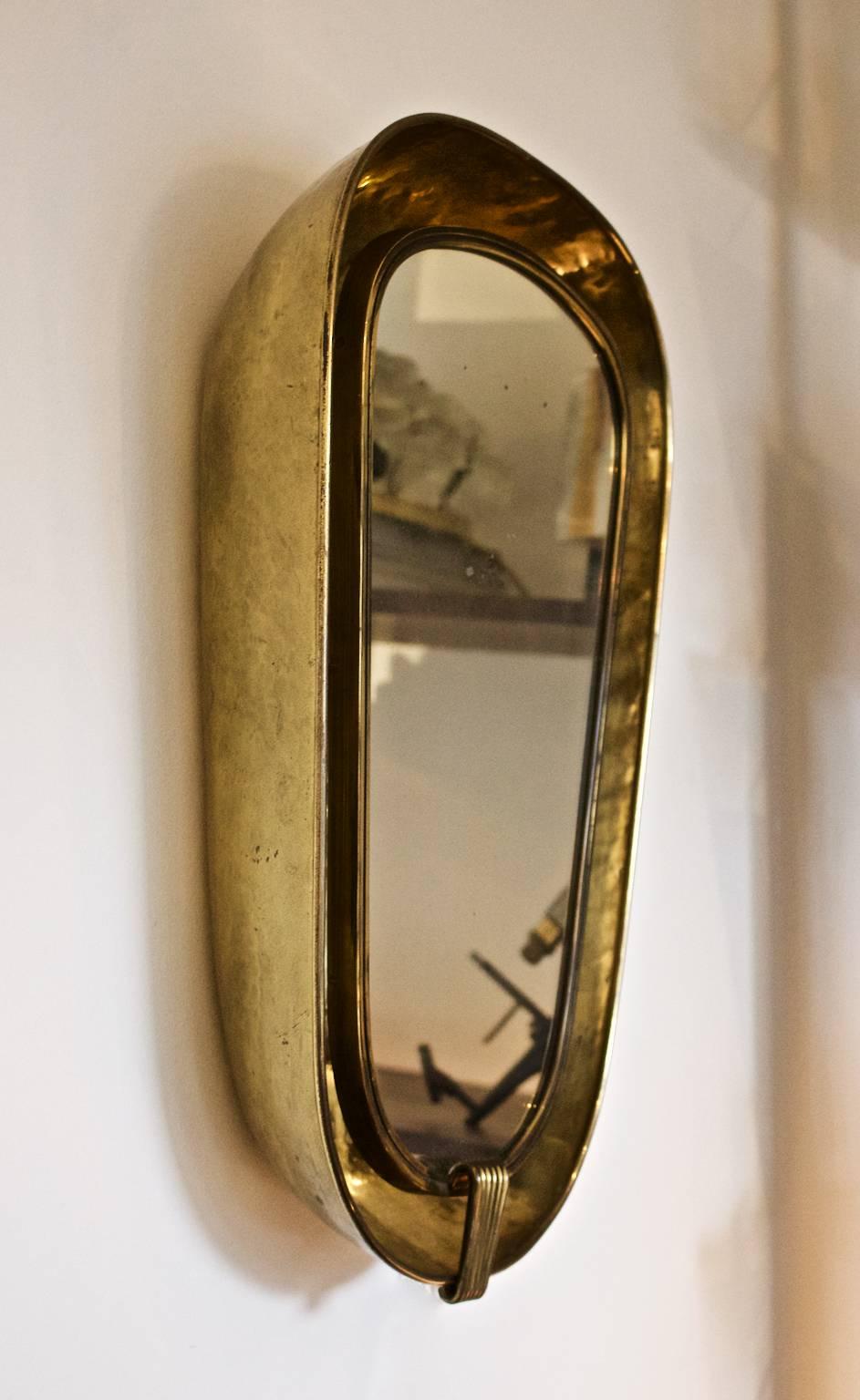 An Art Deco back-lit wall mirror with deep brass frame. European early to mid-20th century.

The brass-framed mirror sits in the centre of a hammered brass bowl and conceals a simple lighting fixture which provides indirect light. The piece is in