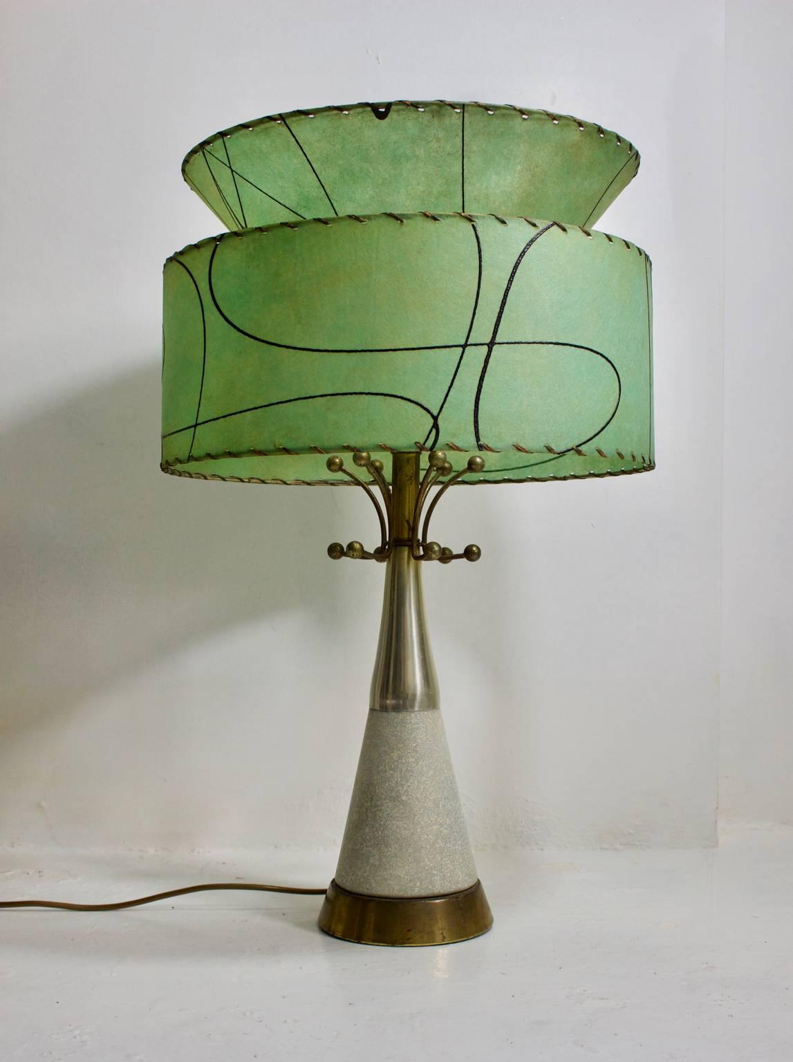 A modernist ceramic table lamp with atomic details, and original fibreglass shade. Probably from the United States, 1950s.

The lamp base sits on a brass base; the center section is ceramic with a grey speckled glaze and the top cone is aluminium.