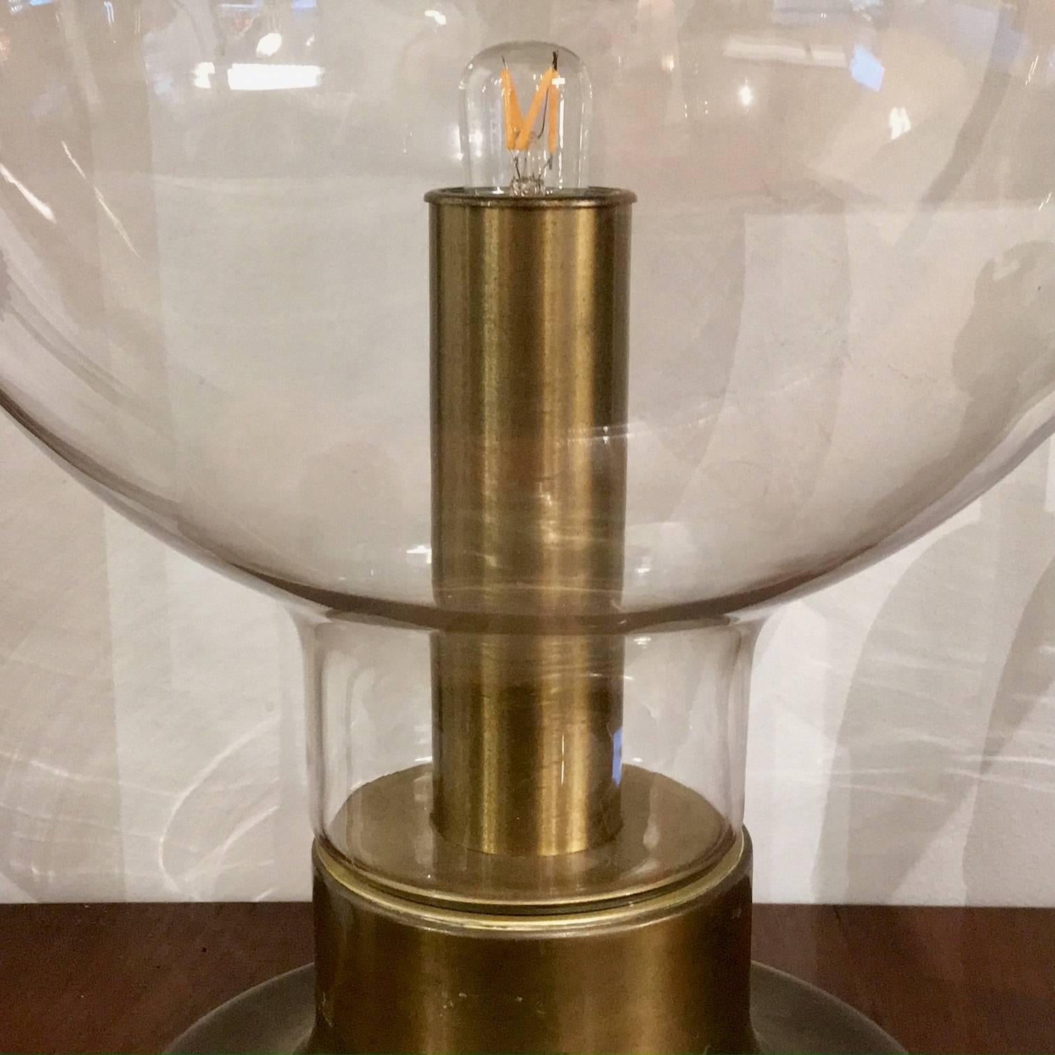 A mid-20th century table lamp in the style of a hurricane lamp. The piece comprises a large open glass bowl, which has a very slight grey tint, over a deep gold coloured interior and a patinated bronzed steel base. Overall it is in very nice vintage