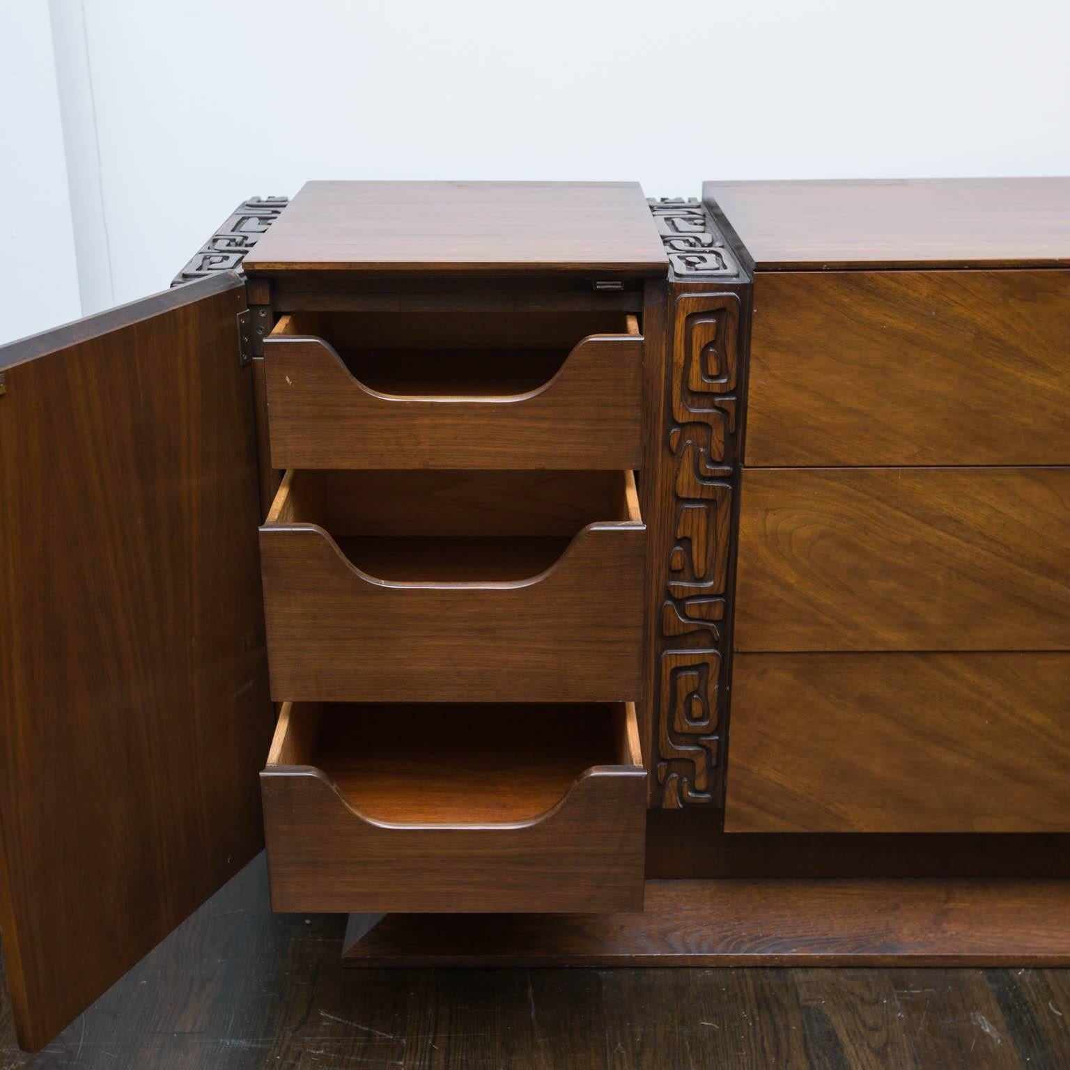 Great example of the Brutalist influence, only with a hint of a south pacific Kon Tiki trim. Bookmatched veneered doors and drawers sit atop a flaired plinth base.