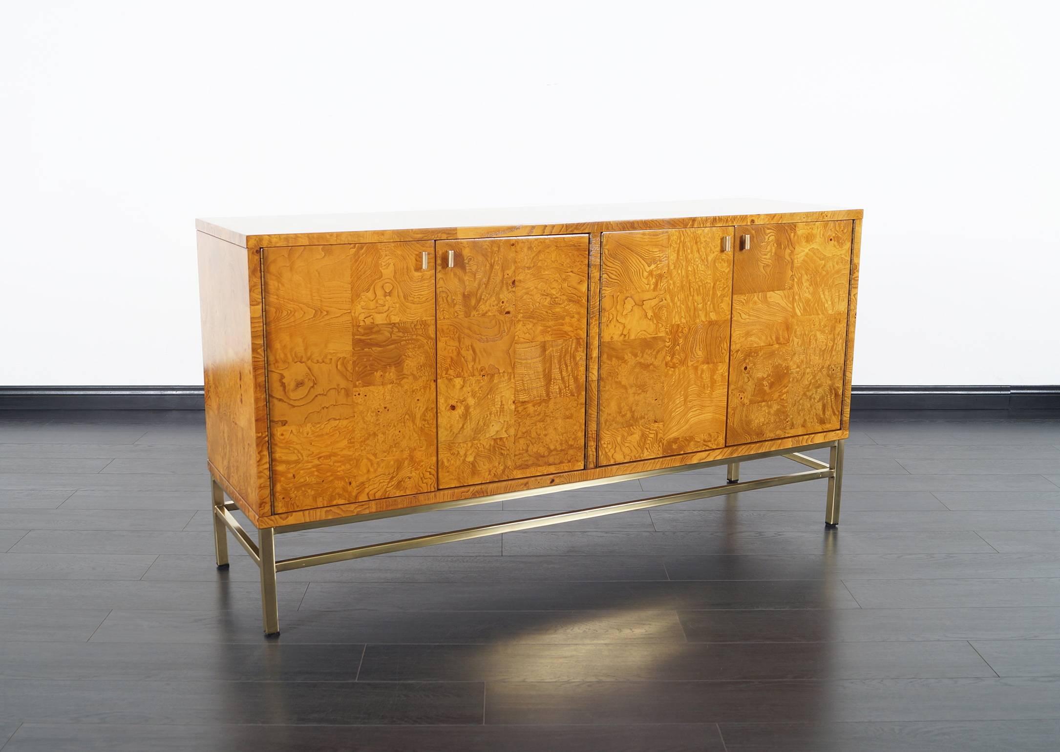 Stunning burl wood credenza attributed to Milo Baughman. Dramatic burl wood case supported by brass base. Features three pull-out drawers on the left and one adjustable shelf on the right side.