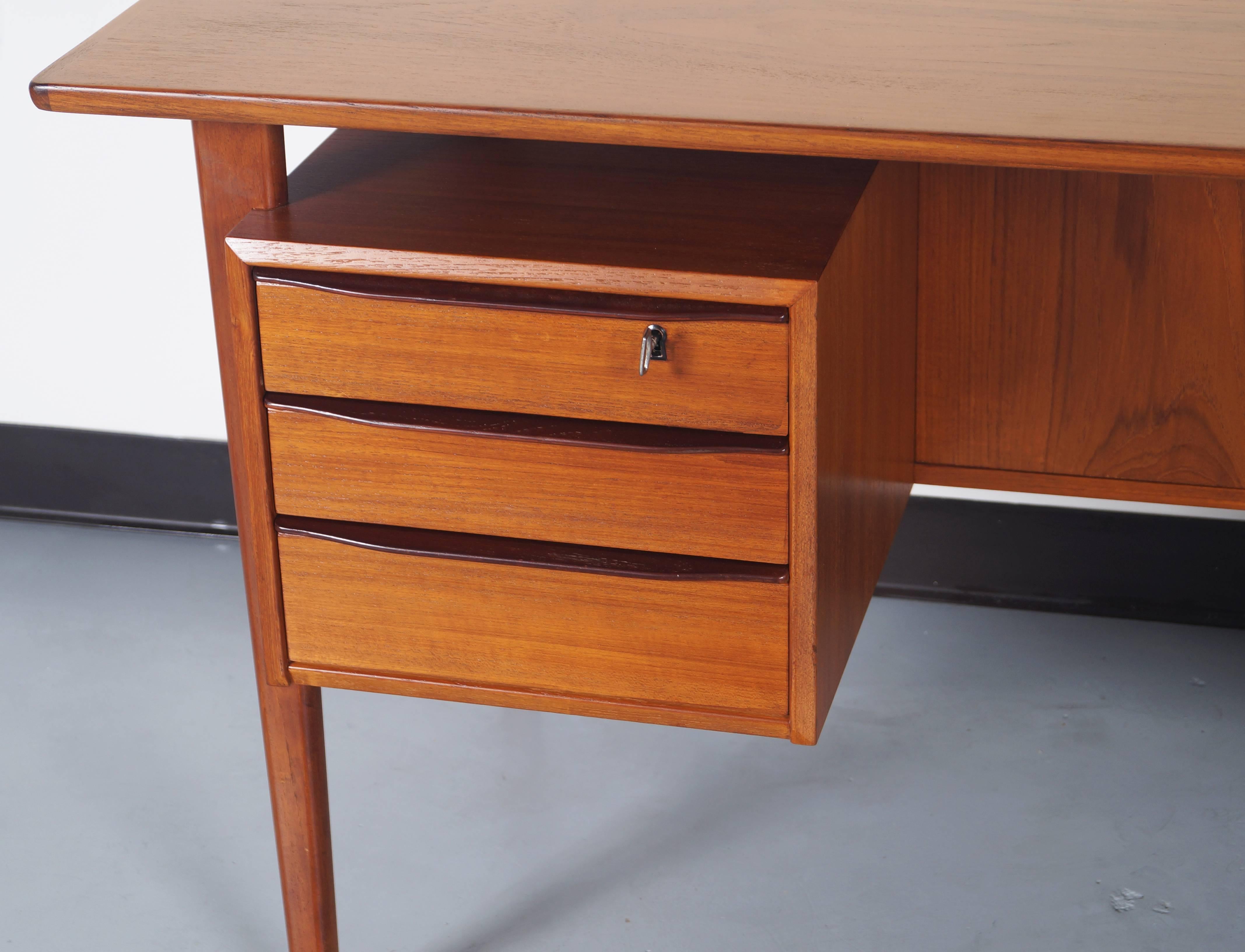 Stunning Danish Modern desk designed by Peter Lovig Nielsen for Dansk Design. Sculptural floating top, raised lips and integrated bookshelves on the back side. Contains four drawers total with a large file drawer. Key included.