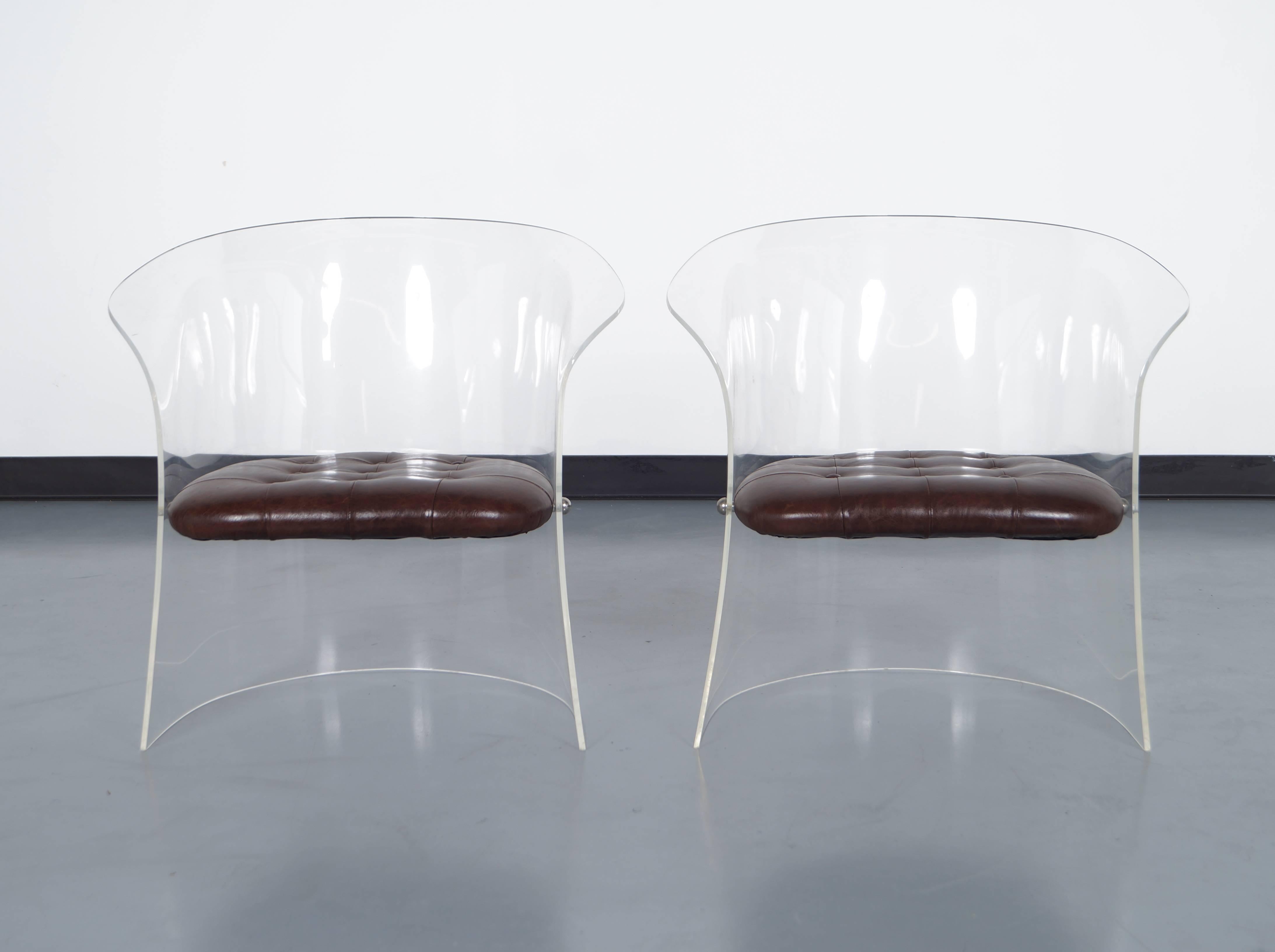 Pair of lucite chairs with tufted leather seats, circa 1970s. The chairs have curved backs and sides and the seats are attached by chrome covers.