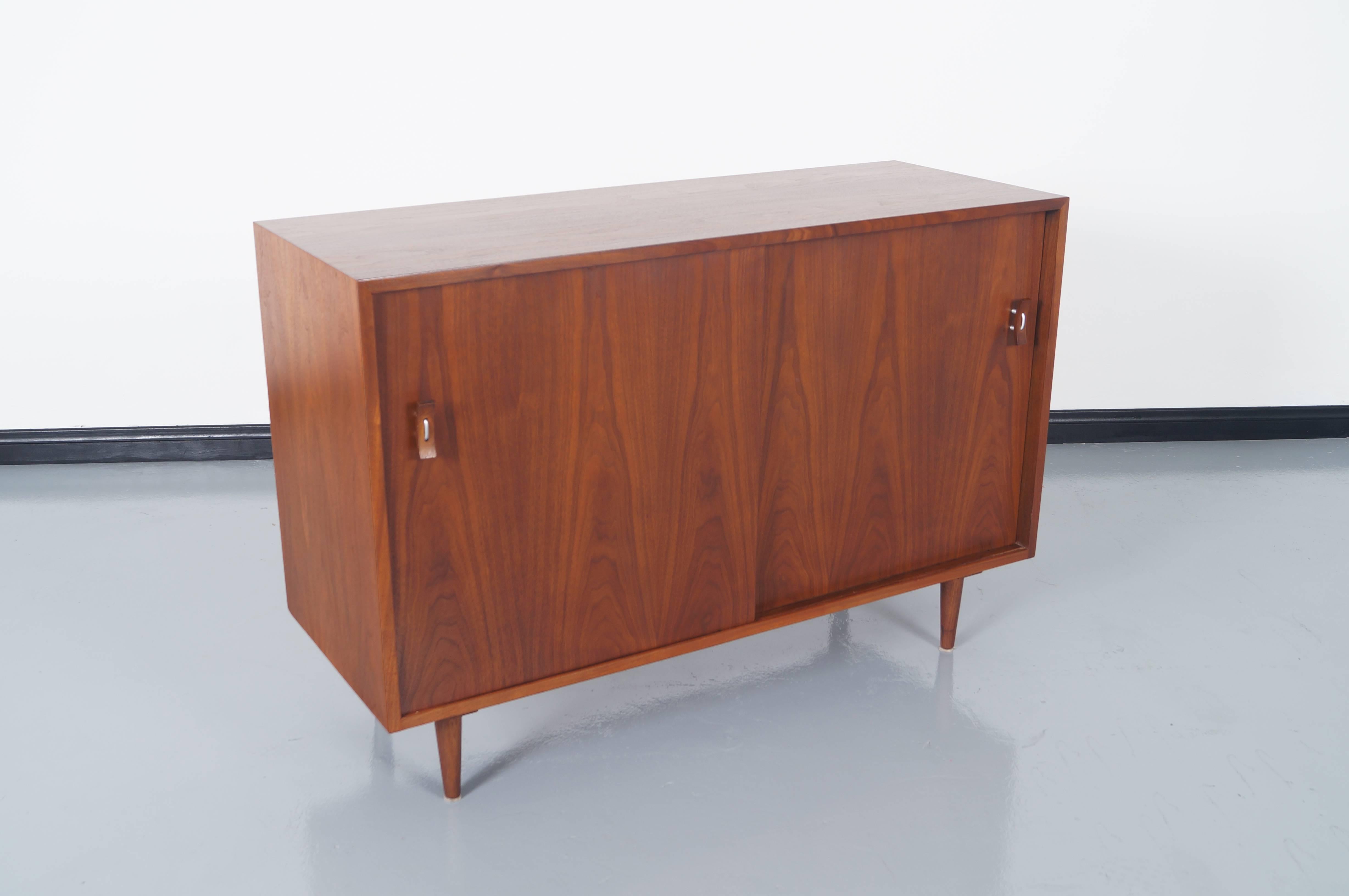 Vintage walnut sideboard by Stanley Young for Glenn of California. It features two sliding doors with sculptural pulls. Inside contains one adjustable shelf on the left side and four lacquer drawers on the right.
