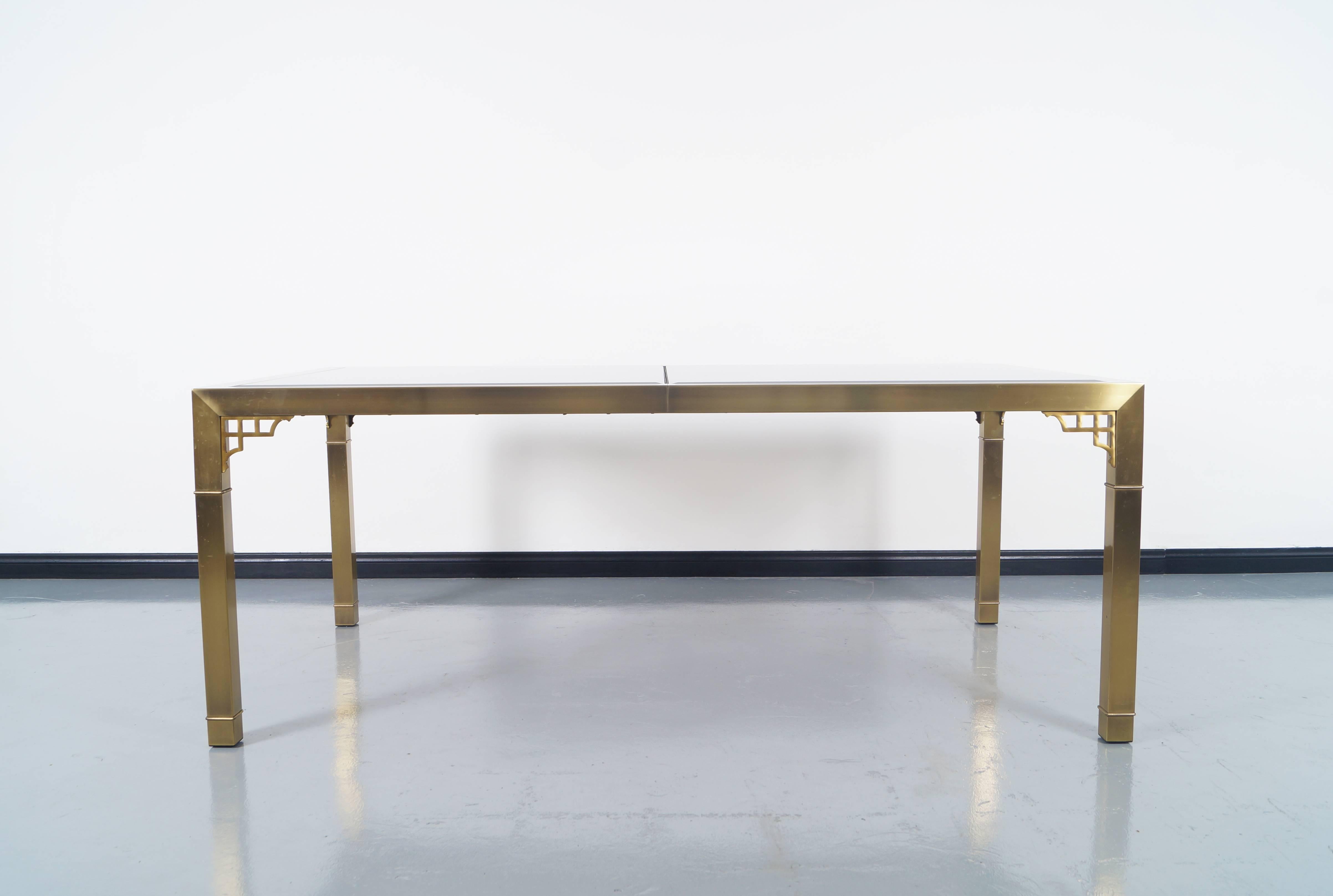 An expandable brass and smoke glass dining table by Mastercraft. This beautiful dining table has one extra leaf. 

Fully extended with leaf 100