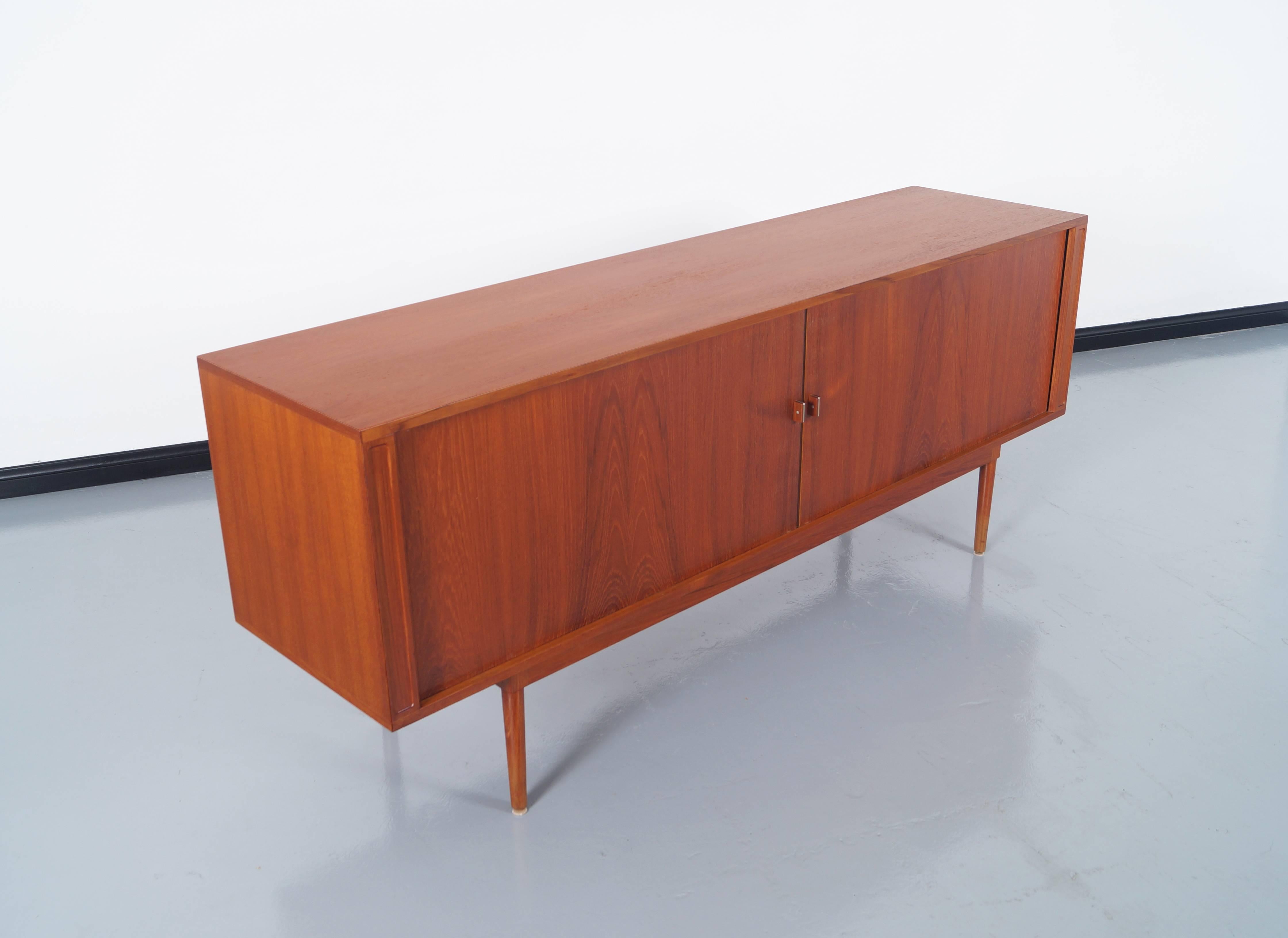 This amazing credenza was designed by Jens H. Quistgaard and manufactured by Lovig Design. Features two tambour door that open to three sections. The middle sections has five adjustable drawers. The section on each end has adjustable shelves.