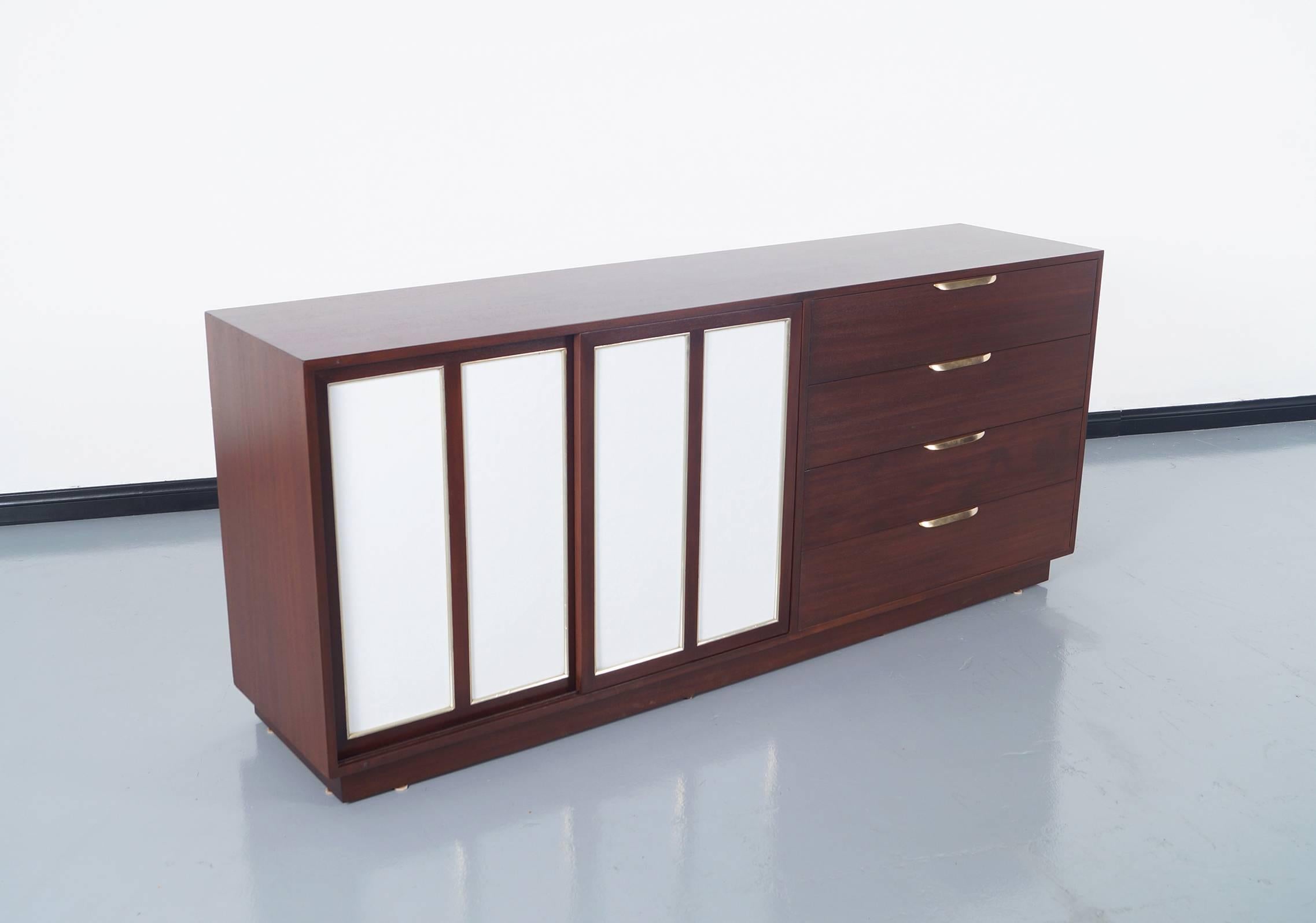 Elegant vintage modern sideboard designed by Harvey Probber in United States, circa 1960s. Features two sliding doors with inset leather on the left side. When opening the sliding doors, we can see a total of eight interior white lacquer drawers,