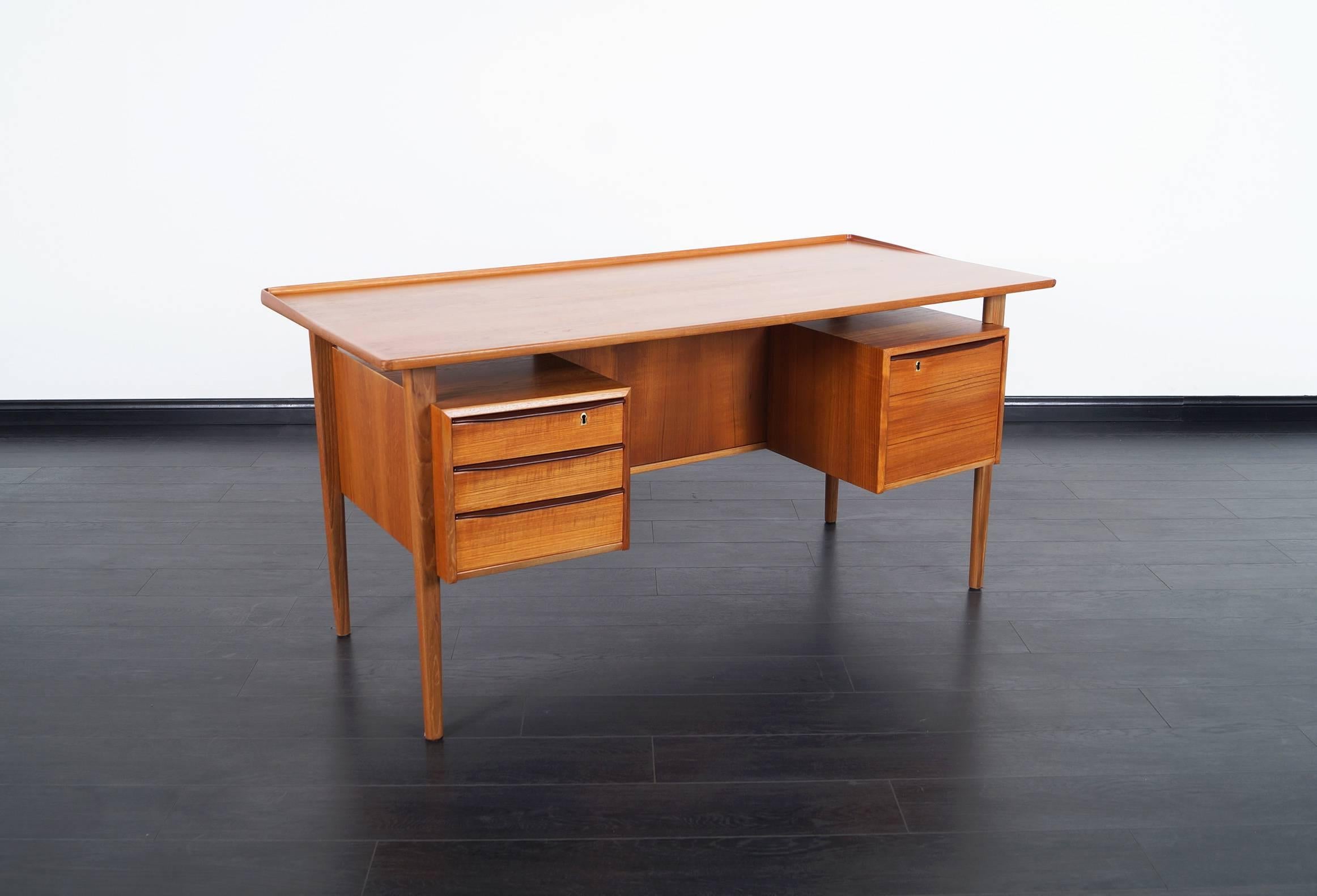Danish modern teak desk designed by Peter Lovig Nielsen for Dansk Design. Features a floating top and integrated bookshelves on the back side. Contains three drawers and a large file drawer.
