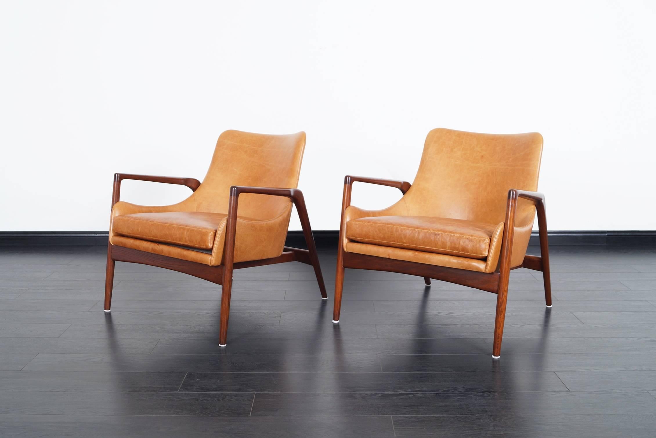 Stunning pair of Danish leather lounge chairs designed by Ib Kofod Larsen. The way the leather shell seems to be floating inside the wooden frame, gives the design an amazing feel from every angle.