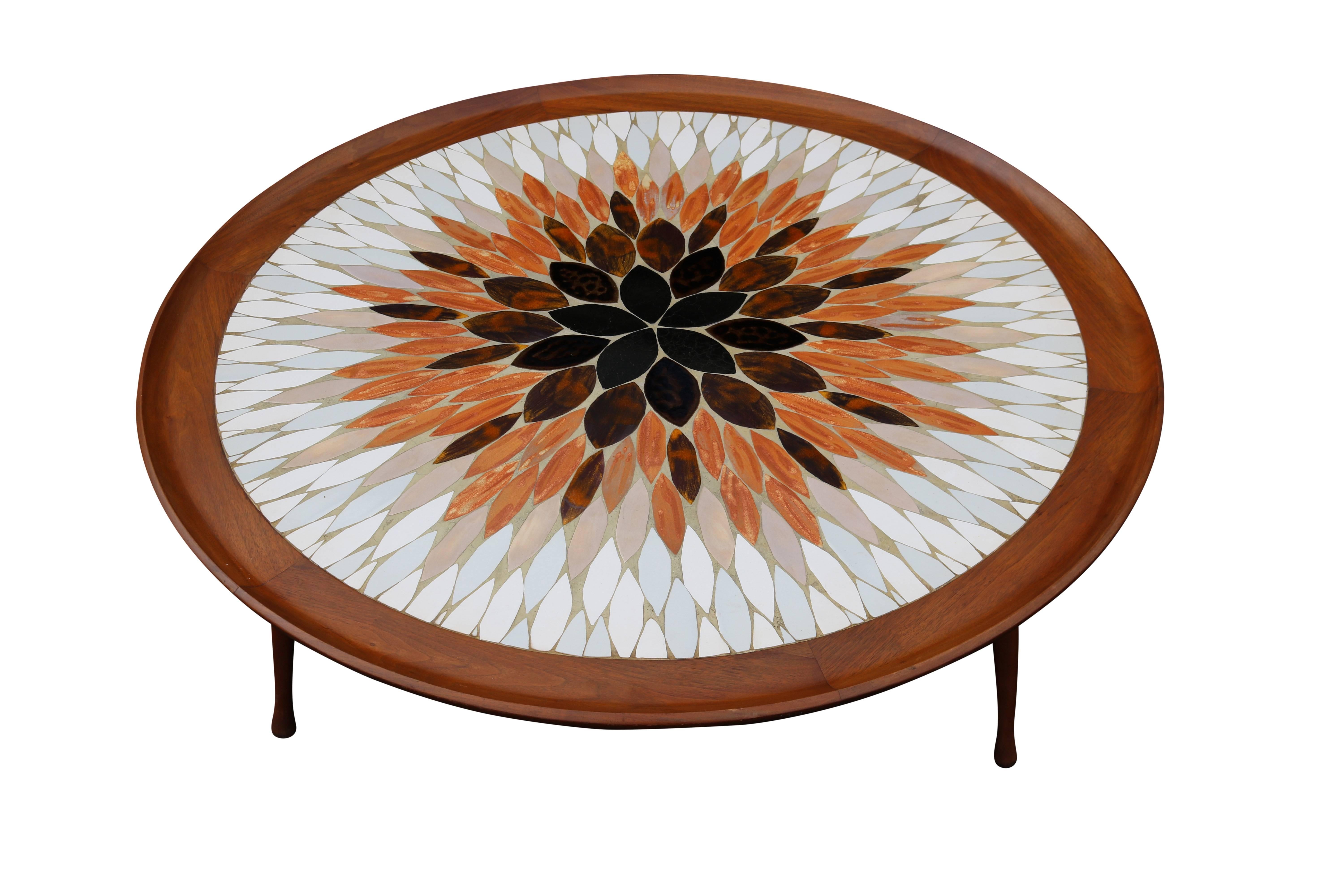 This lovely cocktail or coffee table has a teak base and legs and boasts an intricate inlaid design of leaf shaped tiles in varying colors and glazes. Three legs add to its unique design. Signed 