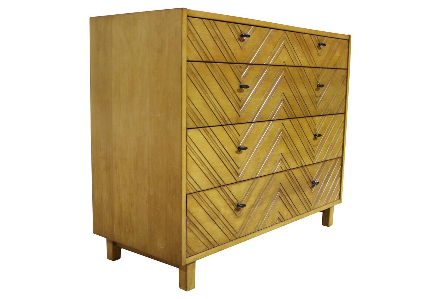 This lovely blonde chest features four drawers with black iron pulls. The front of the chest has been carefully carved with a graphic chevron pattern.