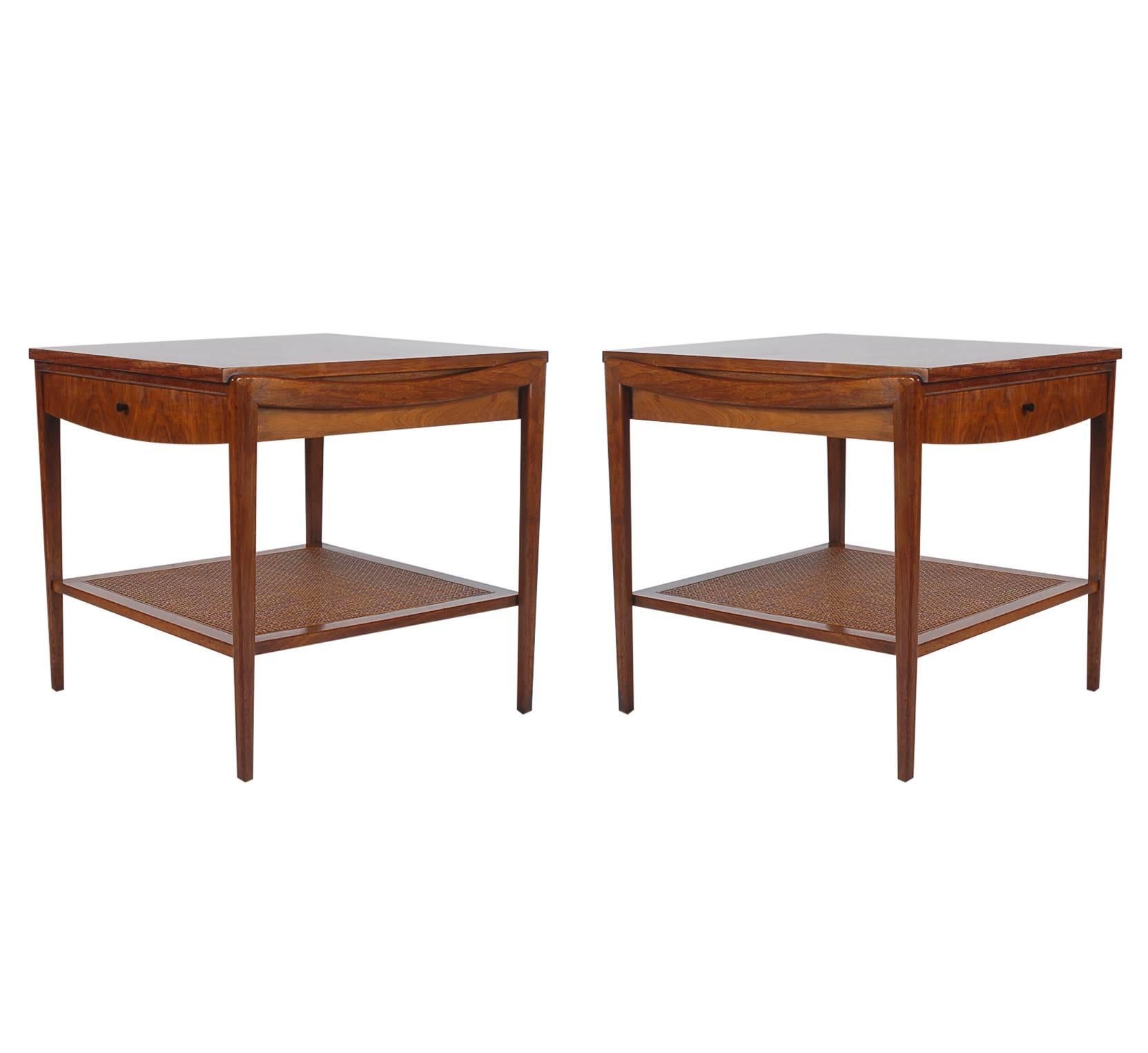 A very simple and handsome designed pair of tables or nightstands produced by John Widdicomb in the 1960s. They feature beautiful walnut construction, single drawers, and a lower tier caned shelf.

In the style of: Ico Parisi, Gio Ponti, Edward