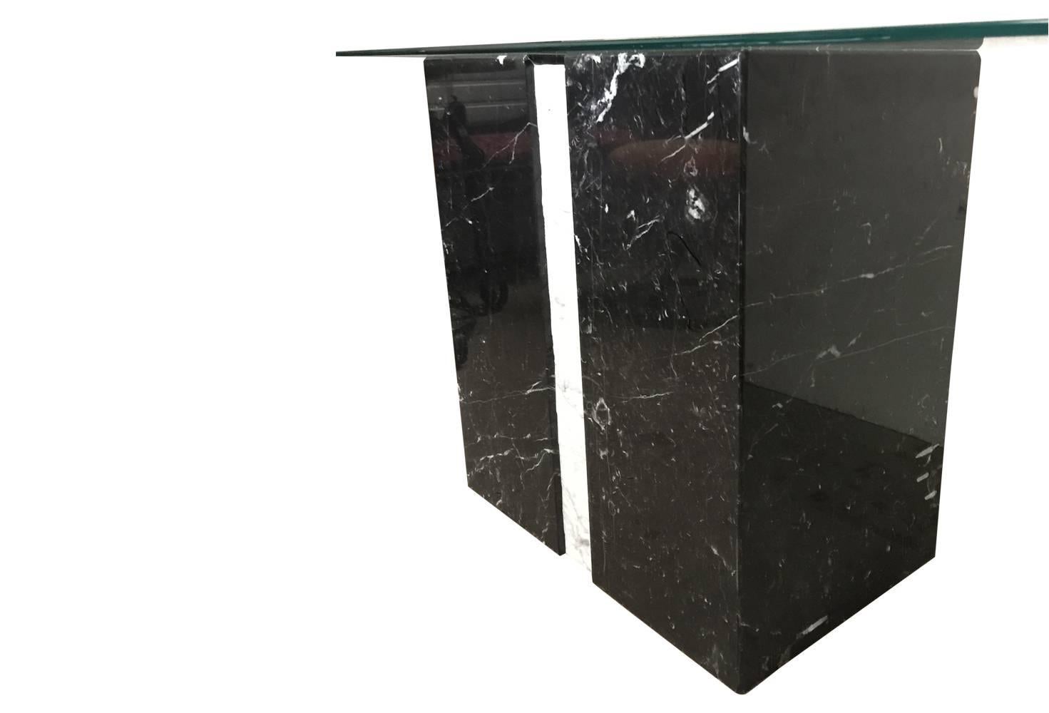This is an awesome table! Base is composed of a stripe of white raw marble nestled between two blocks of polished black marble with white veining. Glass top is beveled and heavy. Awesome piece of postmodern / Hollywood Regency design. 

Measures:
