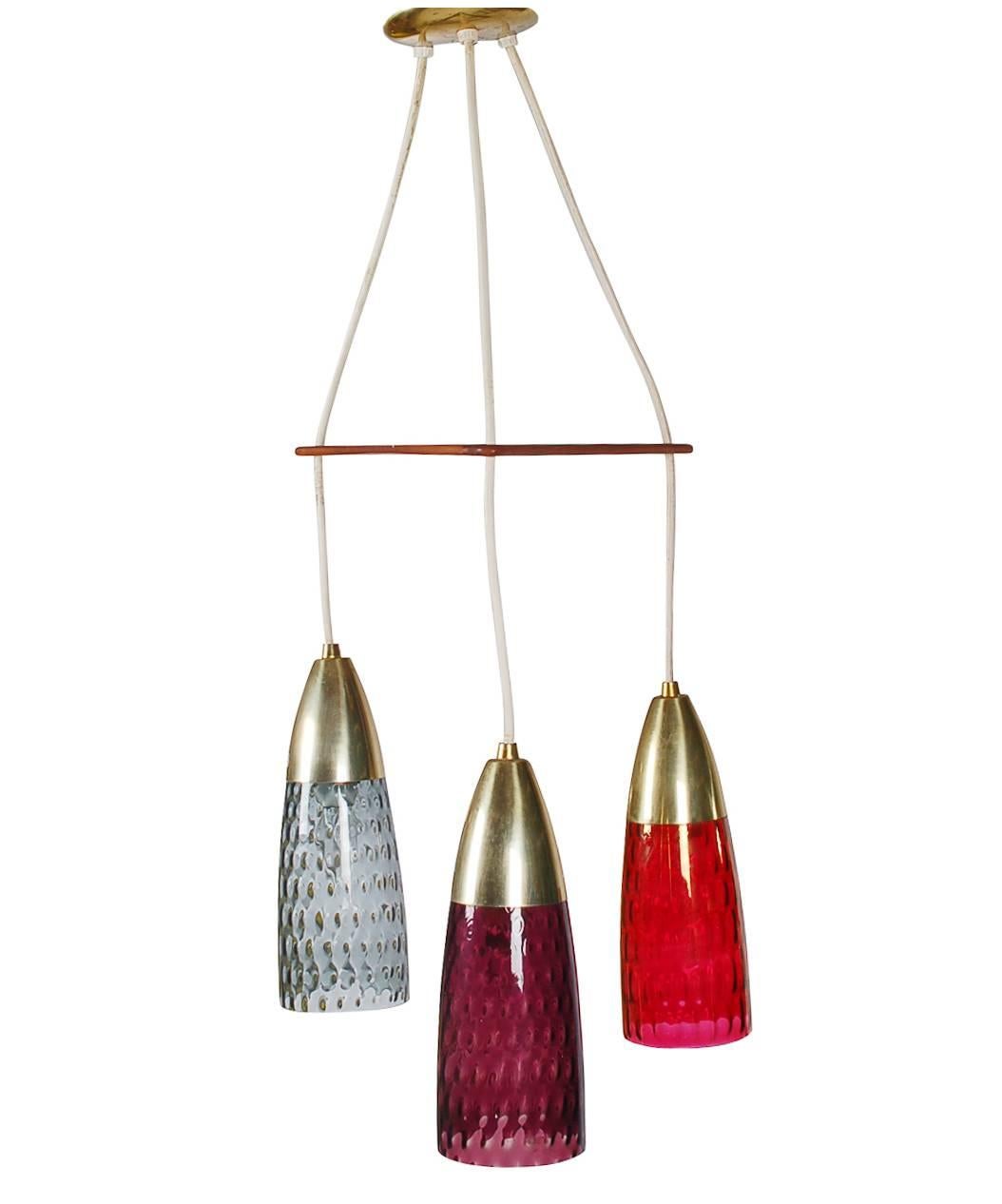 A beautiful hanging lamp that consists of three multicolored glass shades, along with complimentary brass and teak details. Probably Scandinavian made. Each light can be hung at individual lengths (shown at maximum length). Takes three standard