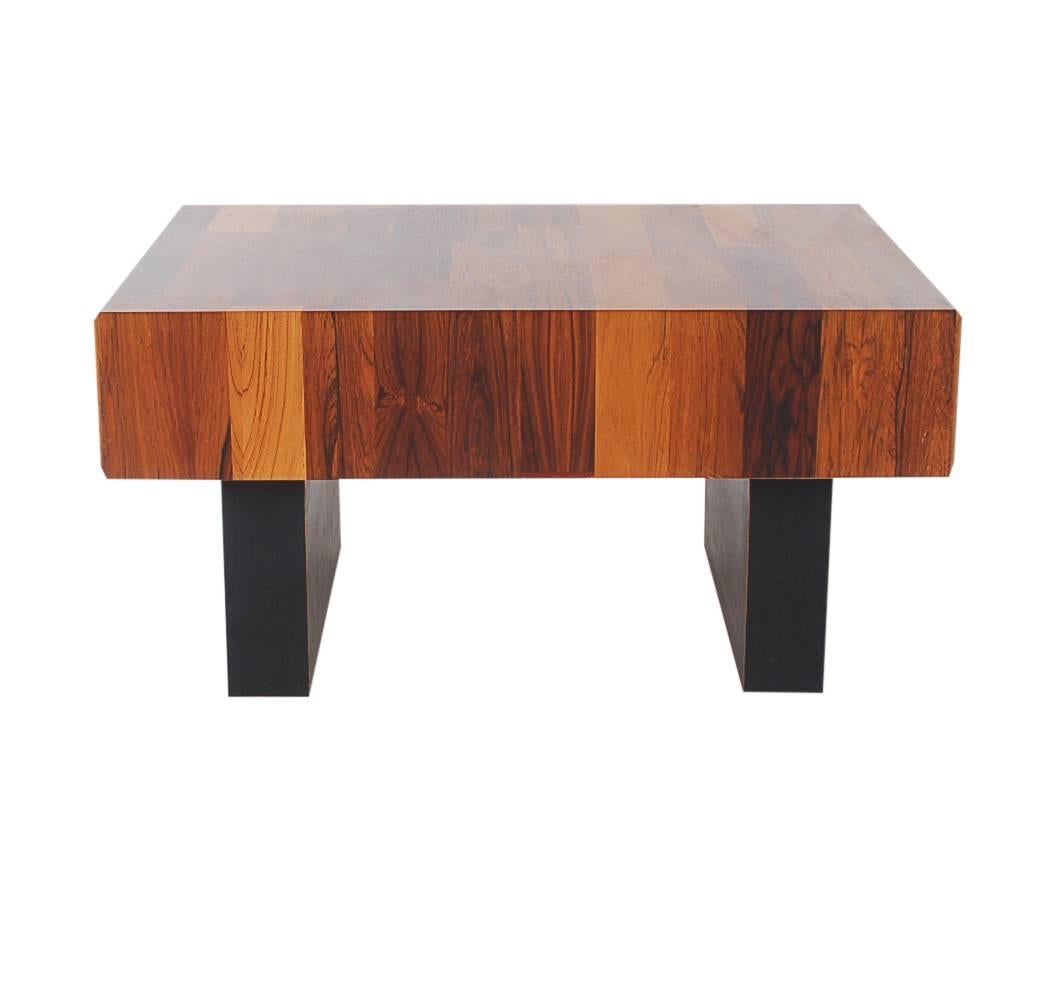 A handsome looking piece that will add some pop to a small space. It features a one sided drawer, chunky black legs, and a mixed wood top.