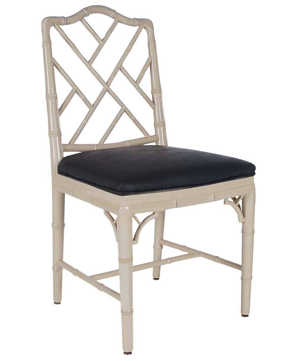 A nicely made set of four faux bamboo Chippendale dining chairs. They feature solid wood frames in a light gray finish with black seat cushions.