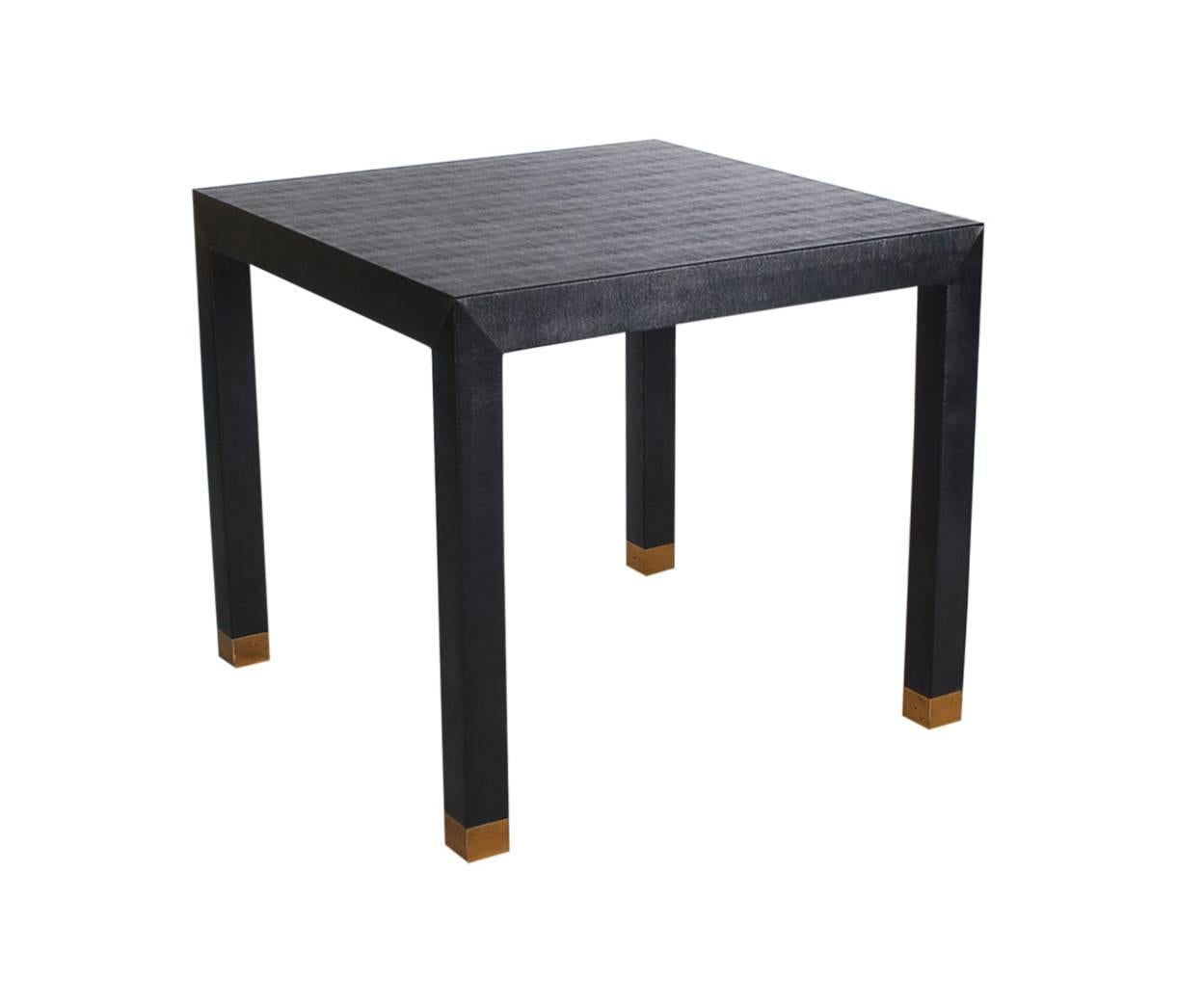 A simple an elegant Parsons design dining table in Black. It features brass capped legs, covered in black snake skin print Naugahyde. 

In the style of: Karl Springer or Milo Baughman.