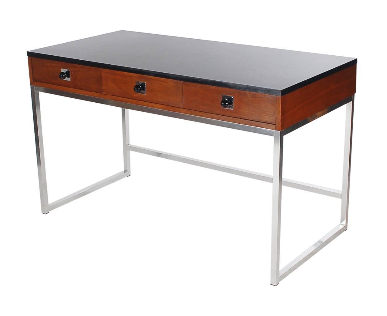 A handsome American modern desk, circa 1970s. It features a chrome base with a walnut and black laminate top. 

In the style of: Milo Baughman.
