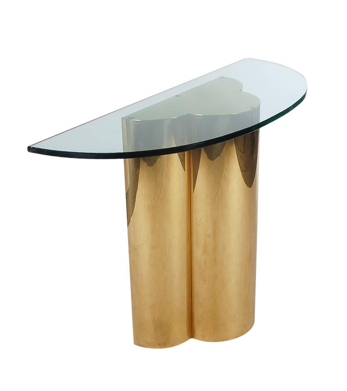A beautiful trefoil form console table after C. Jere. It features a sculptural brass base, with thick demilune cut-glass.