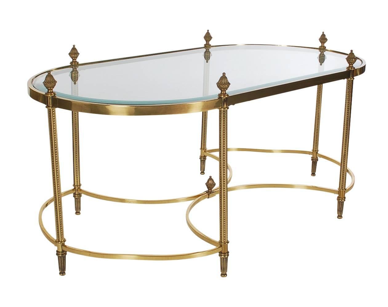 A lovely looking decorative table in the French style after Maison Jansen. It features a brushed brass frame, inlaid glass and finial designs.