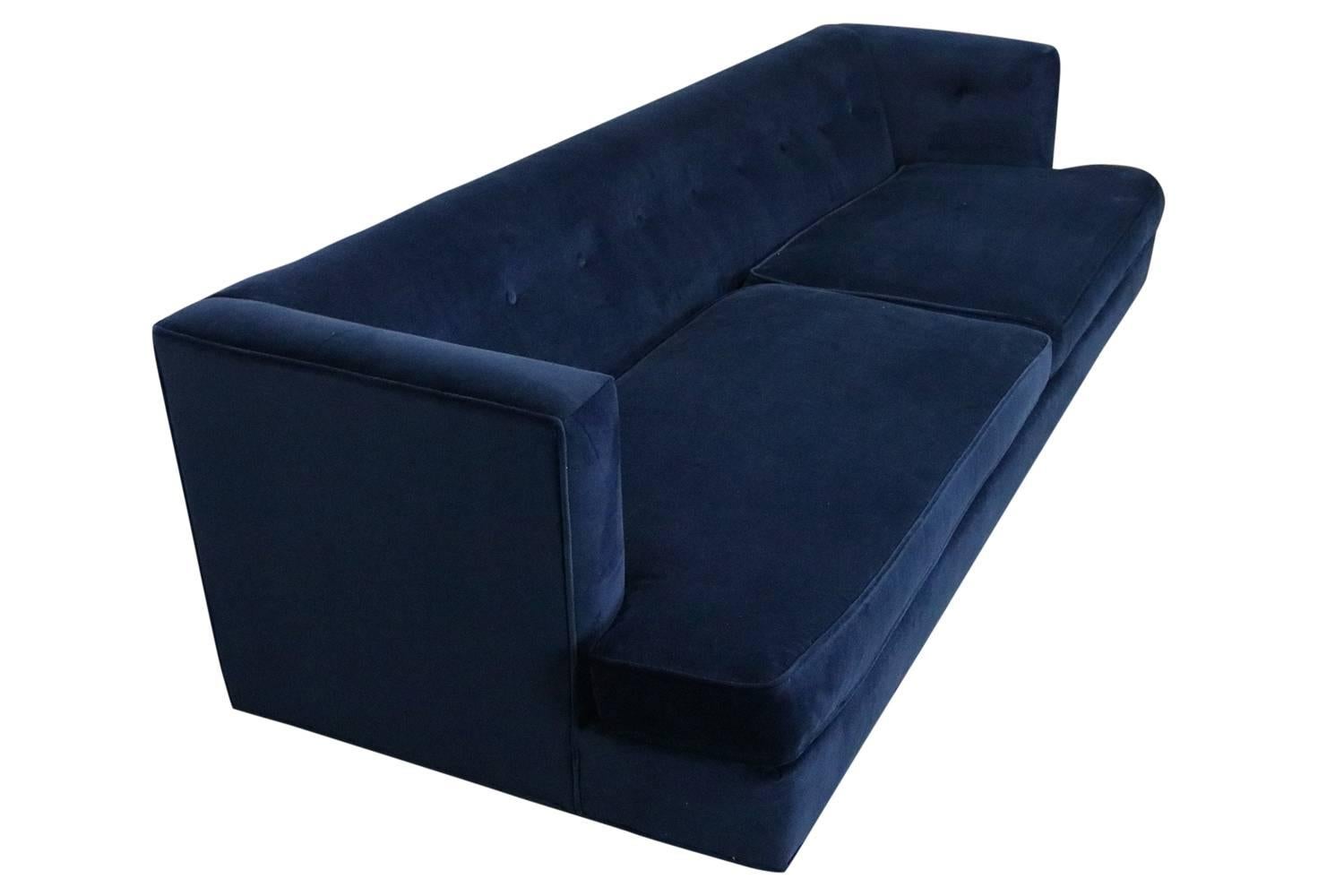 Long and lean and fully restored, this gorgeous sofa is covered in a soft navy blue velvet and has rich walnut legs.