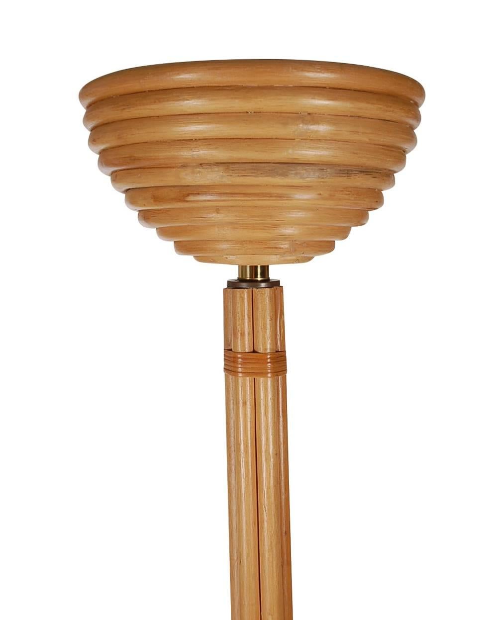 A uniquely designed torchiere in an Art Deco form in the manner of Paul Frankl. It features a rattan construction with a patinated brass base. It takes two standard bulbs, and is in full working order.